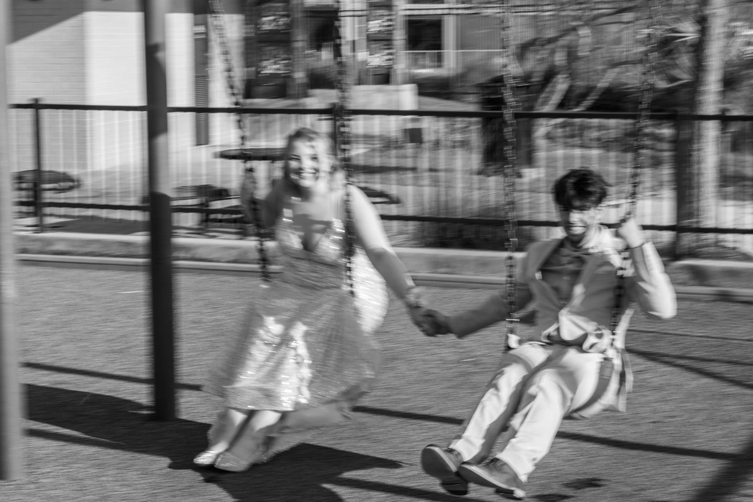 Two children swing side by side on a playground swing set in this vintage black and white photograph.
