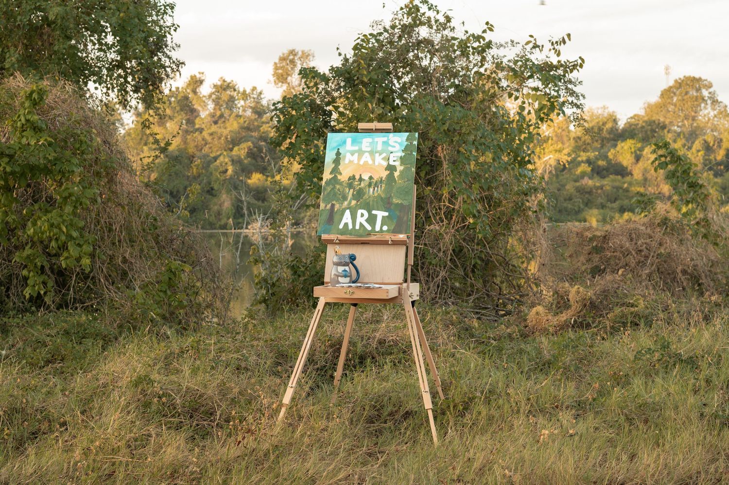 A rustic wooden art easel stands in a grassy field with trees in the background during golden hour.