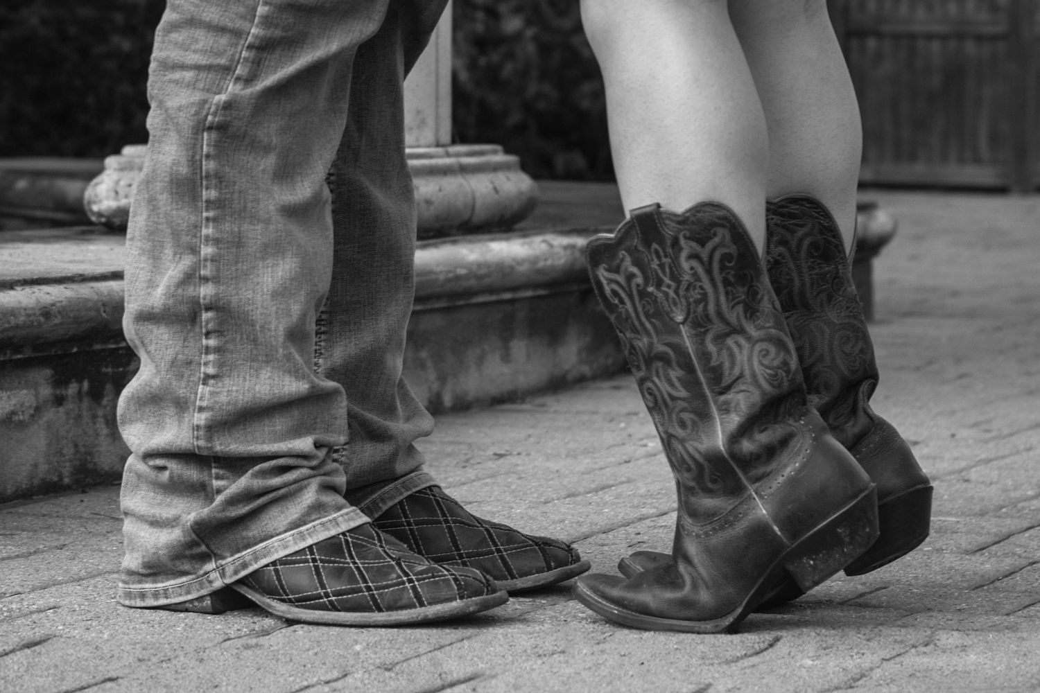 Black and white photo of a couple wearing denim jeans and cowboy boots standing close together on stone steps.