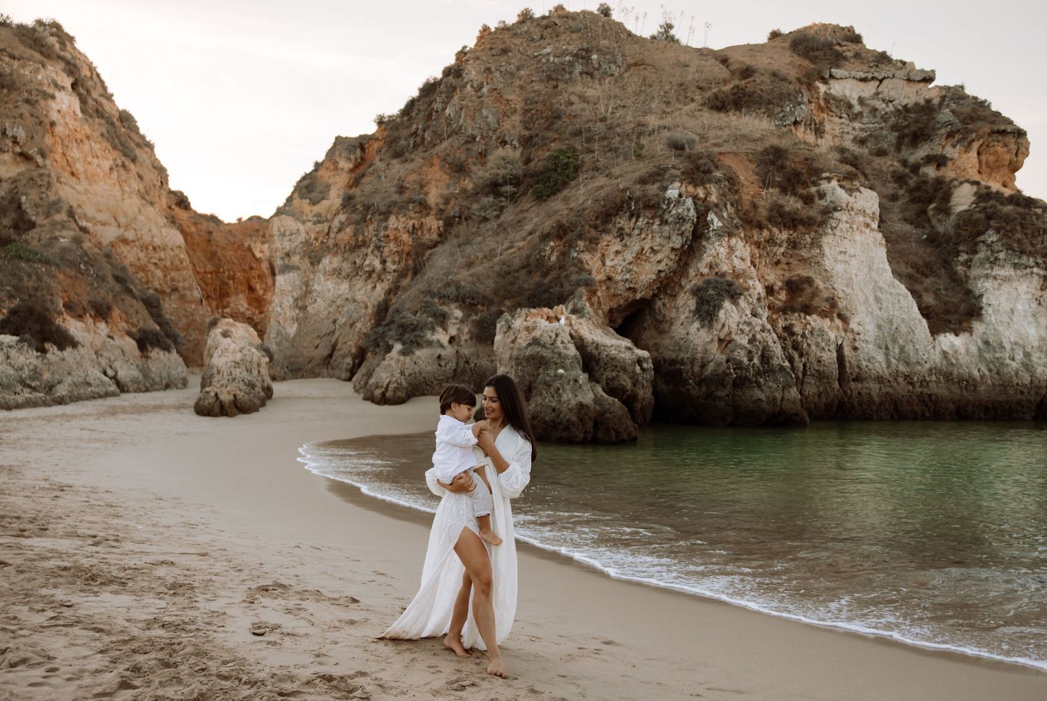 Romantic beach scene with rocky cliffs and ocean waves in the background.