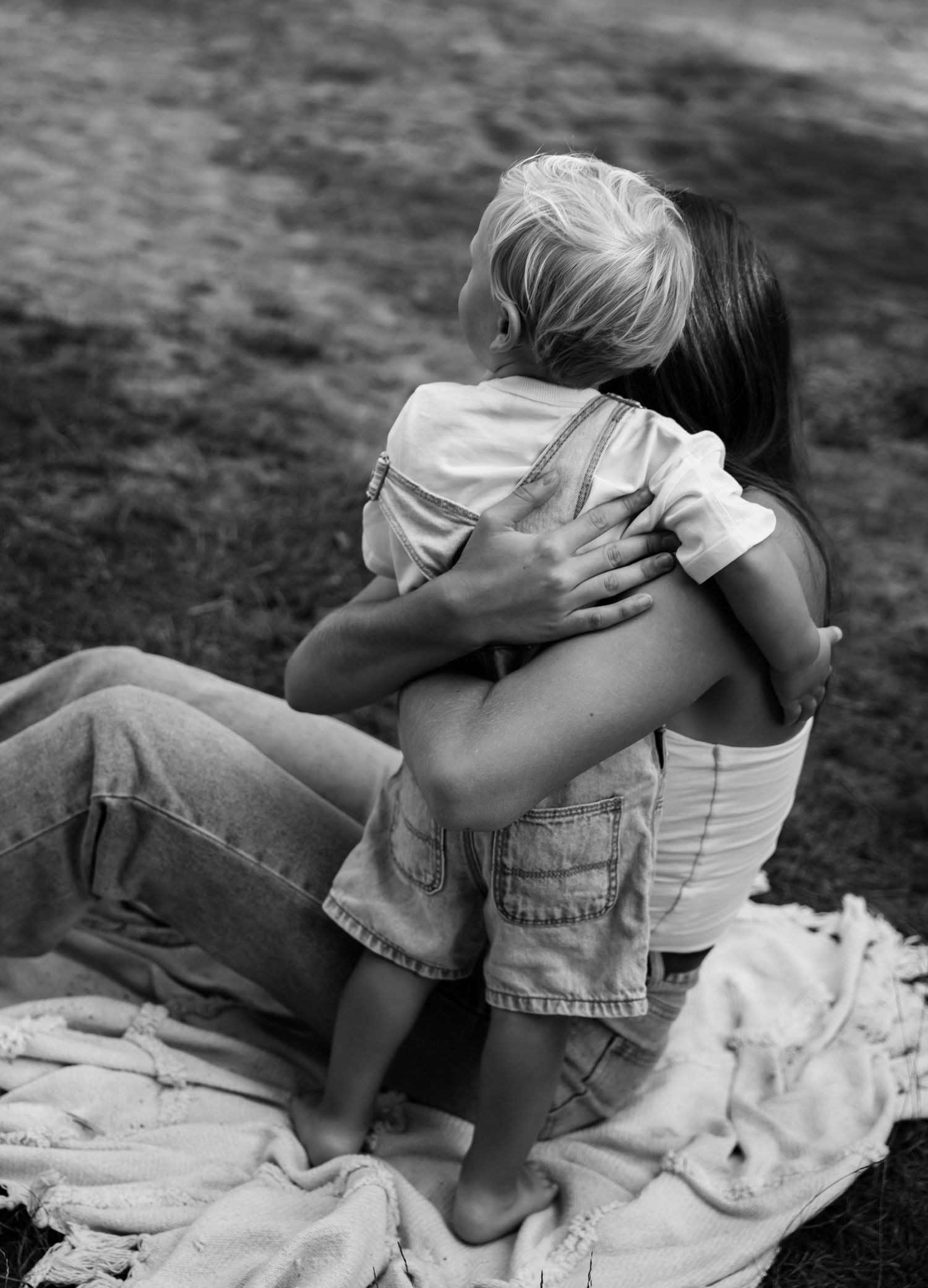 Black and white photo capturing an intimate embrace between parent and child outdoors.