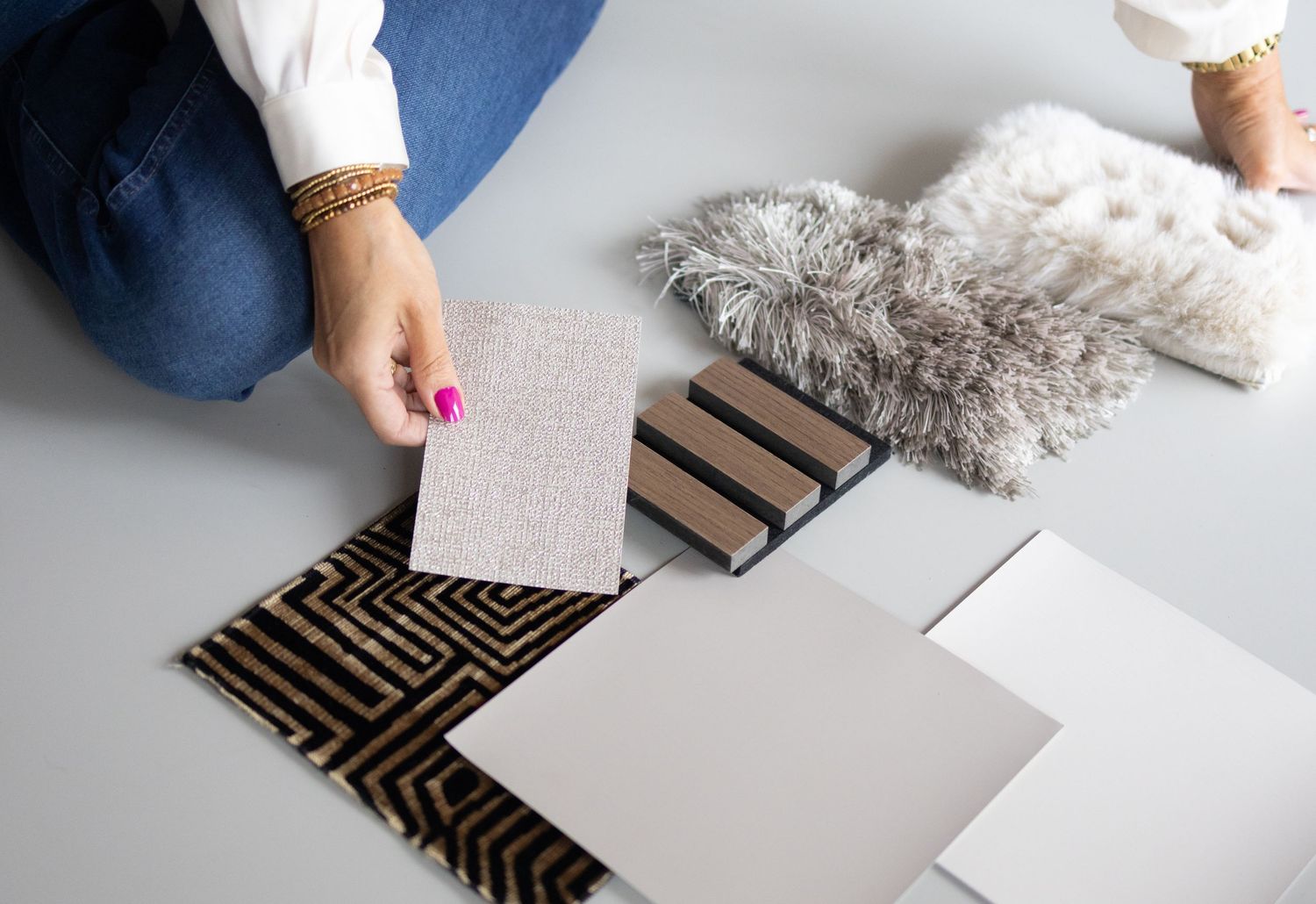 Overhead view of hands arranging fabric and material samples on a white surface.