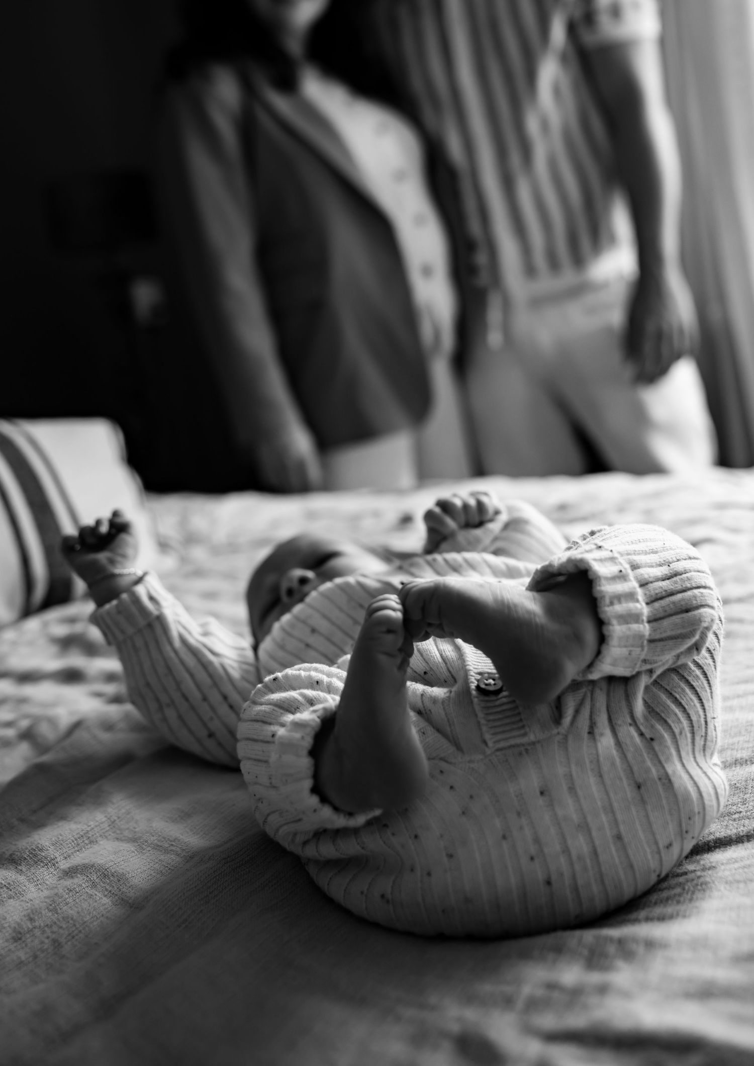 Black and white image of a baby in knitted clothing lying on a bed.