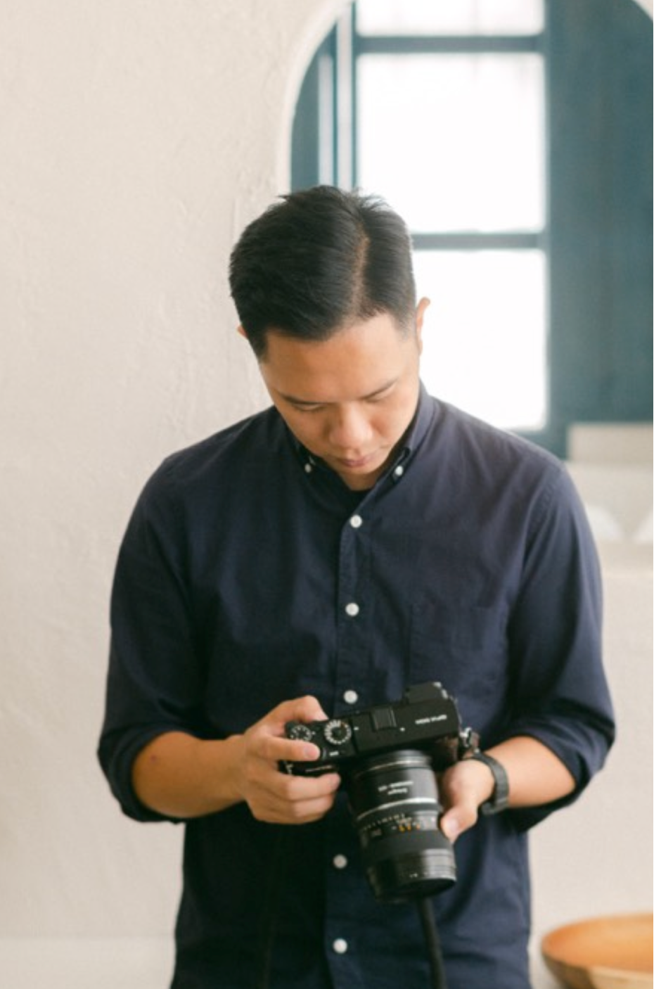 A man in a navy blue shirt examines a professional DSLR camera indoors near a window.
