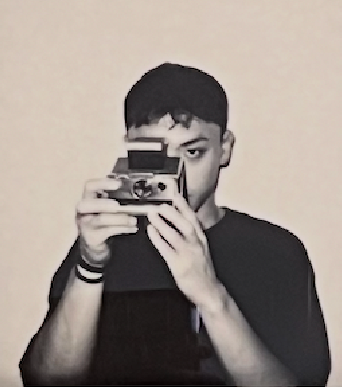 Young man holding a vintage Polaroid camera up to his face in a black and white artistic portrait photo.