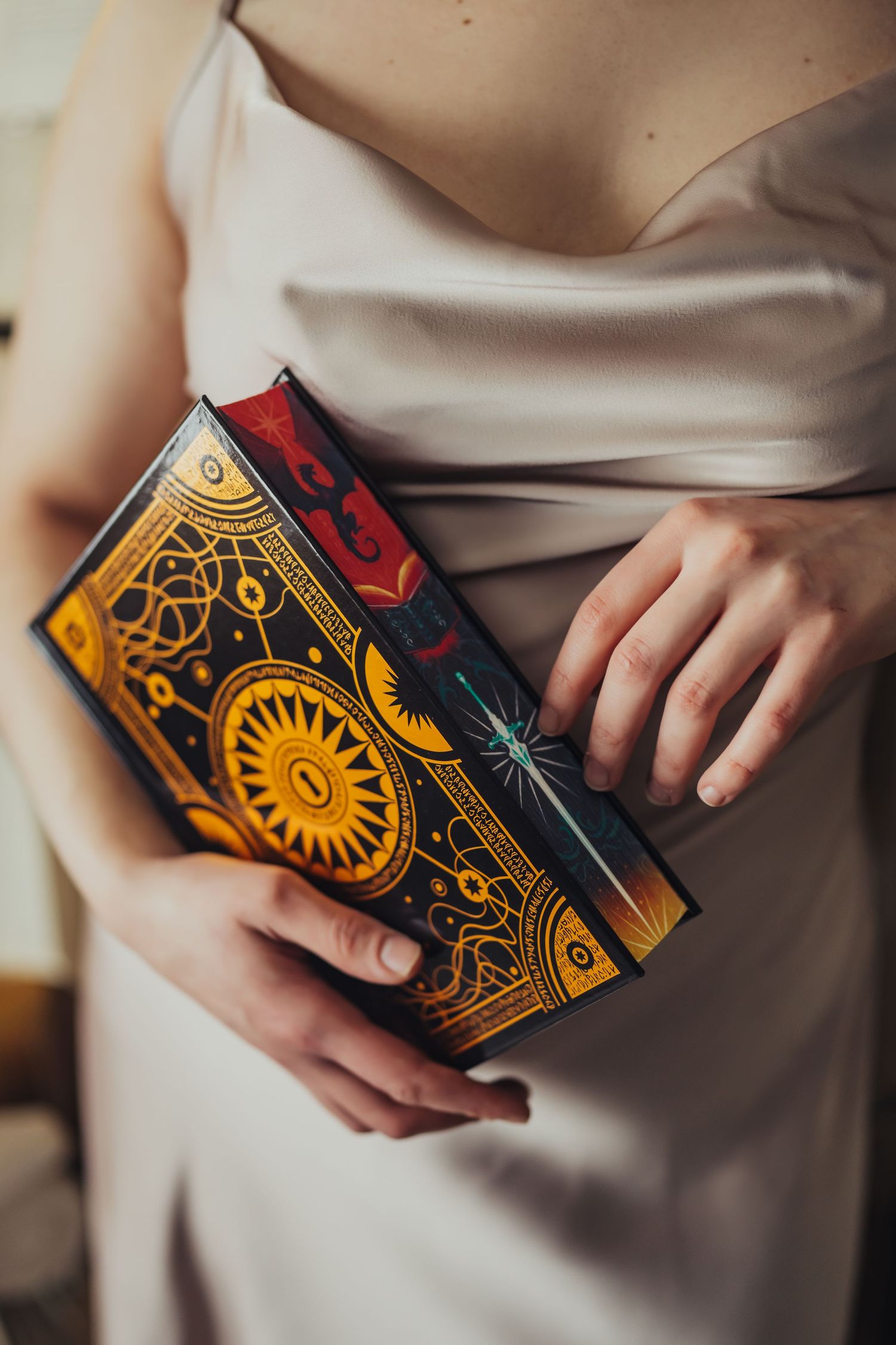 Close-up of a woman in a satin dress holding an ornate gold and navy hardcover book with celestial designs.