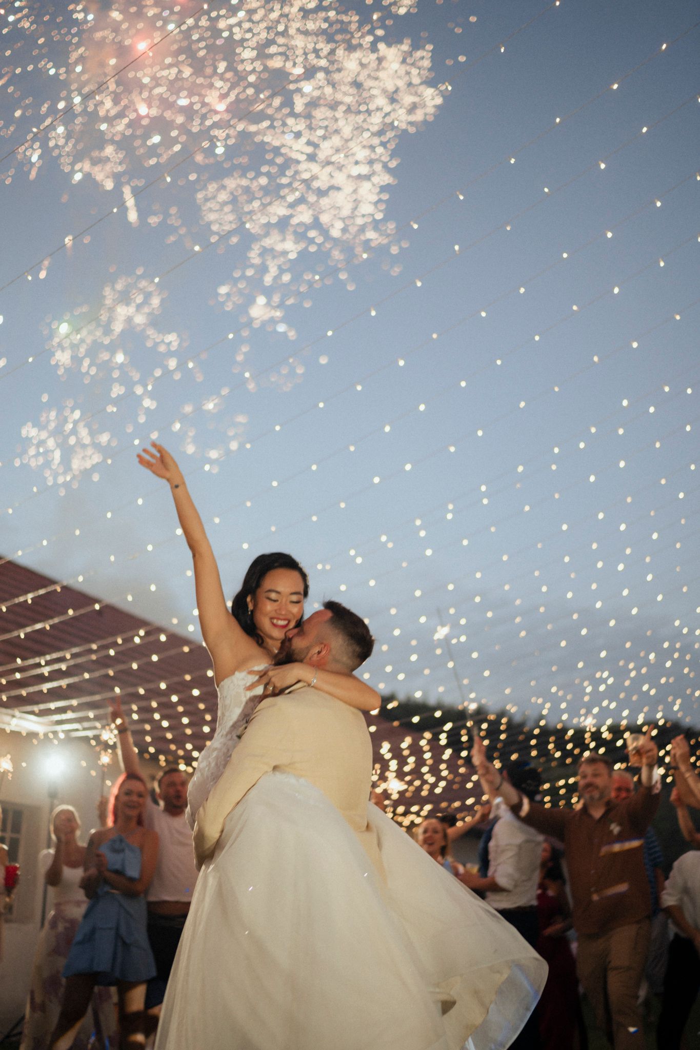 Wedding celebration under twinkling string lights with dancers and sparklers creating magical ambiance.