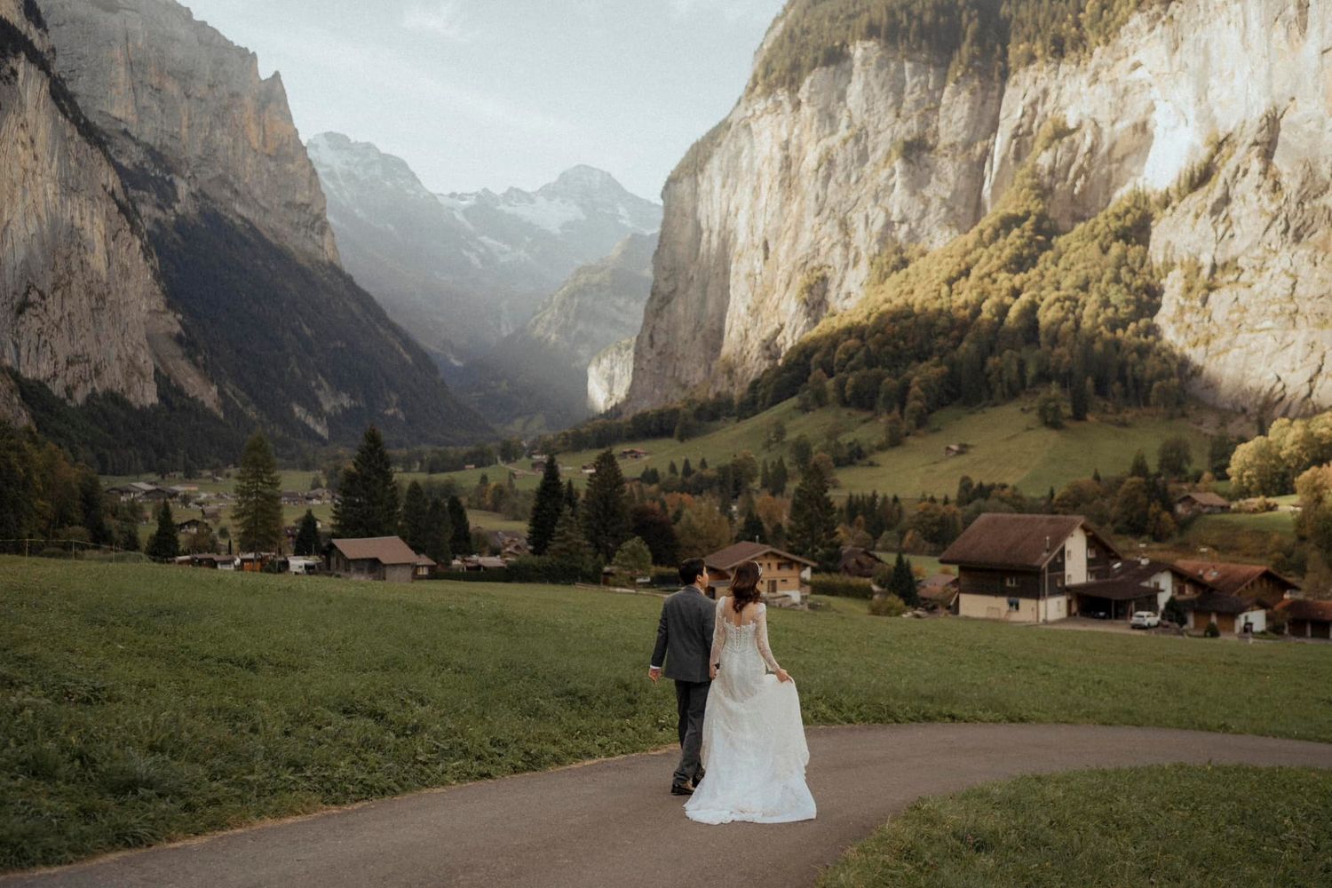 A scenic wedding photo in front of towering mountain cliffs and a small alpine village in Switzerland.