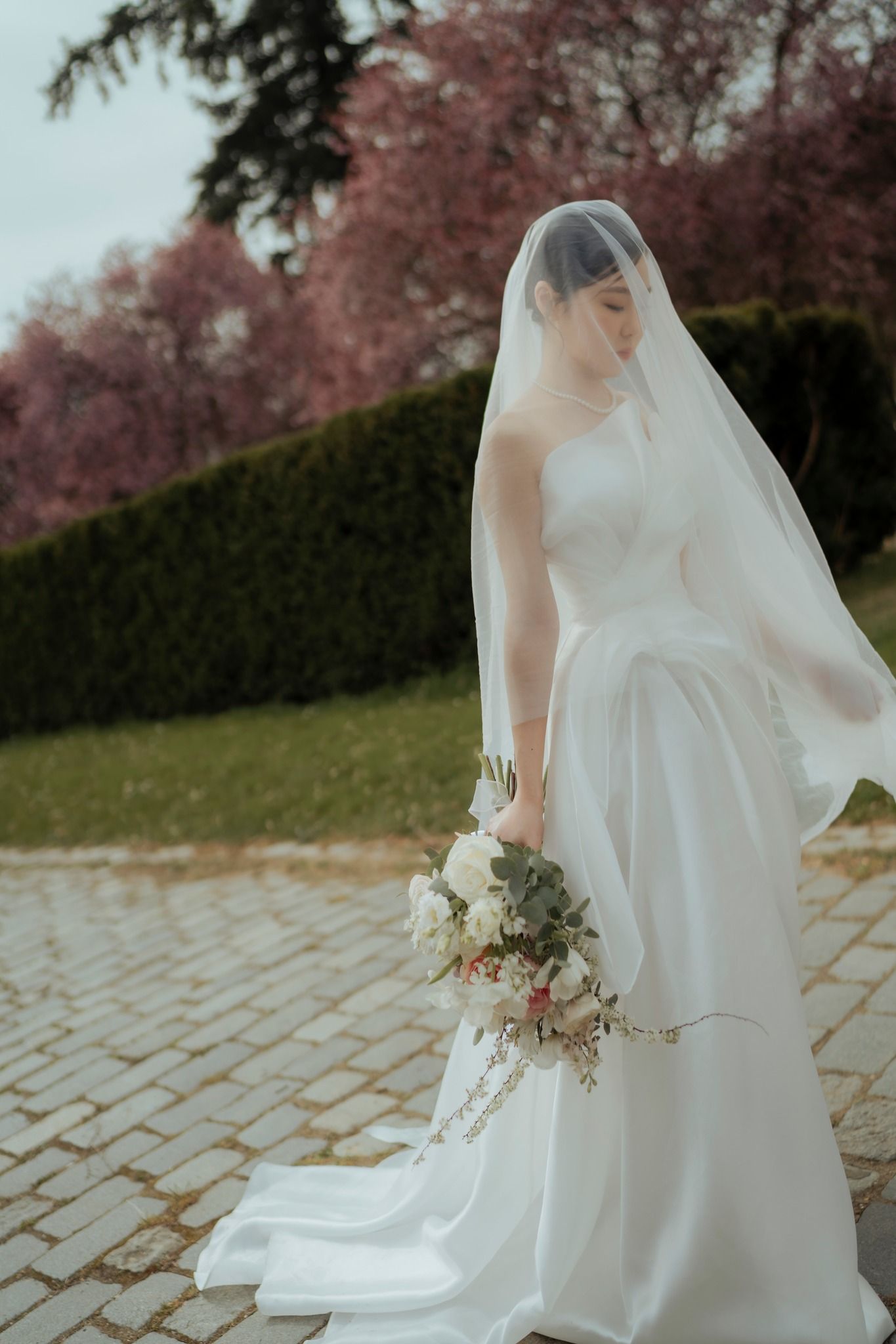 Elegant white wedding dress with flowing veil photographed against blooming cherry trees.