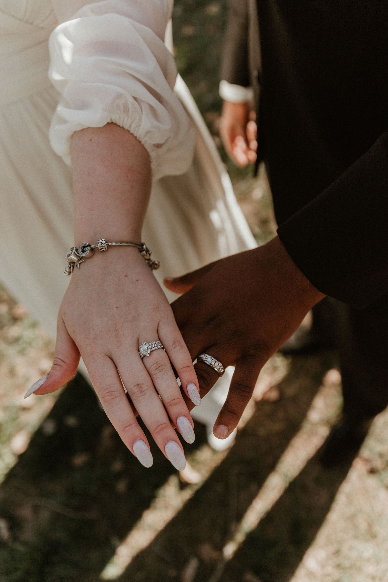 Close-up shot of intertwined hands displaying wedding rings and jewelry.