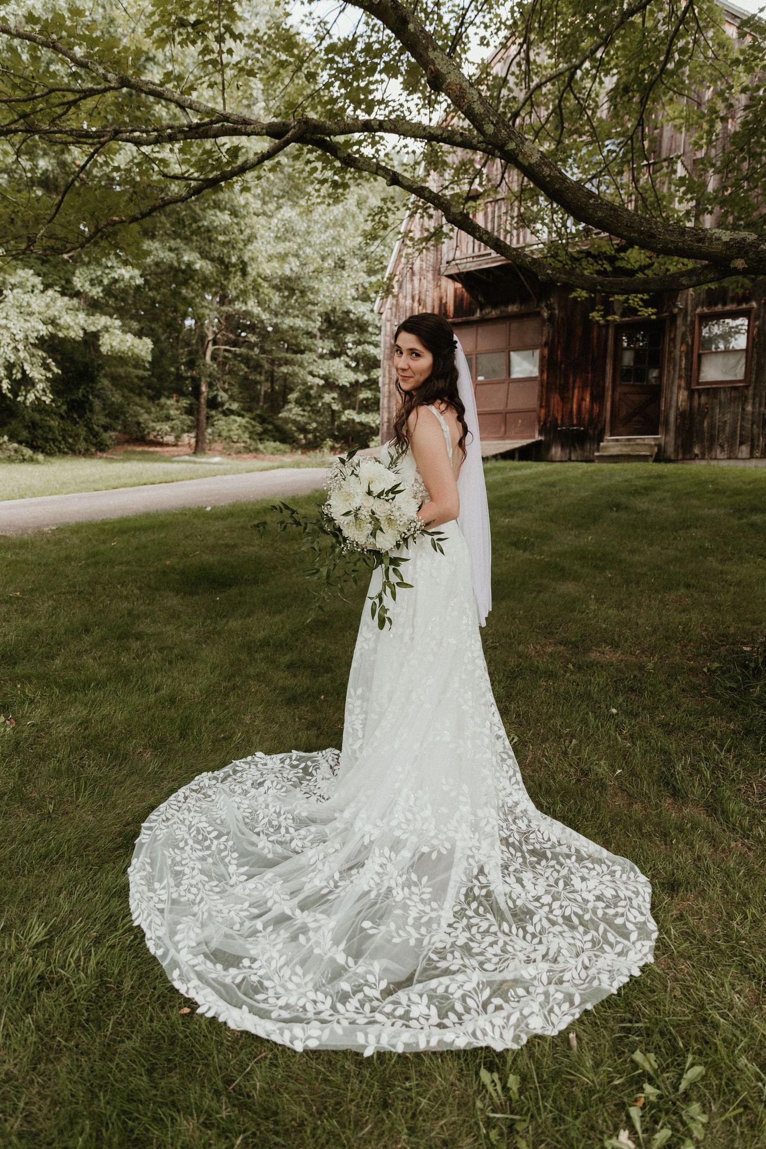 An elegant lace wedding gown with intricate train details captured on a grassy lawn under trees.