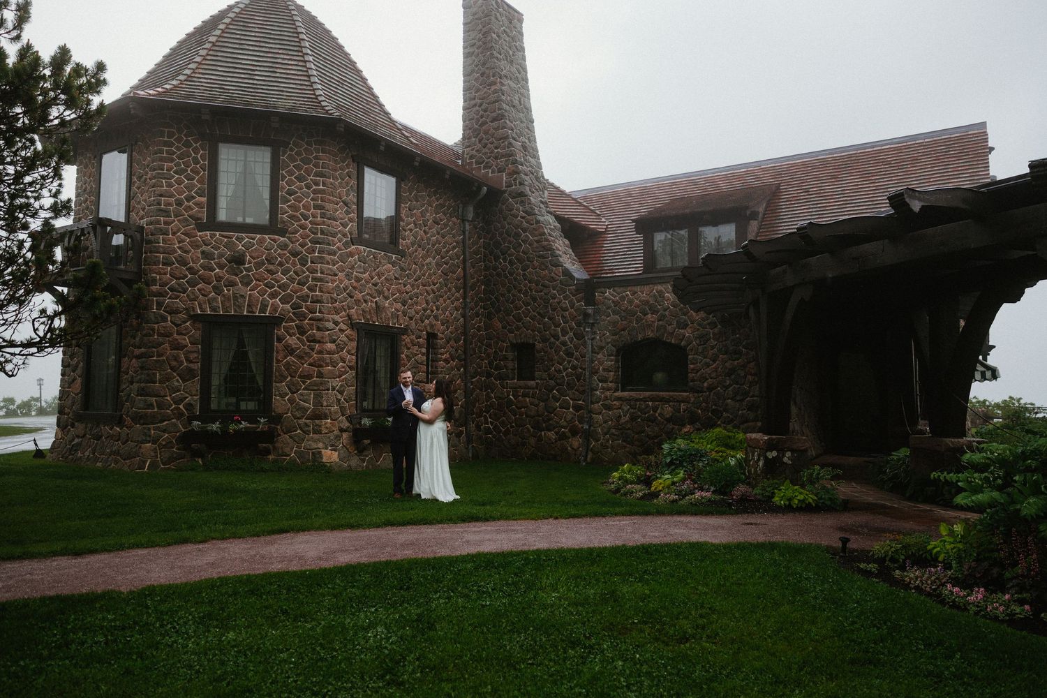 Stone building with conical tower sits atop grassy hill overlooking scenic landscape at dusk.