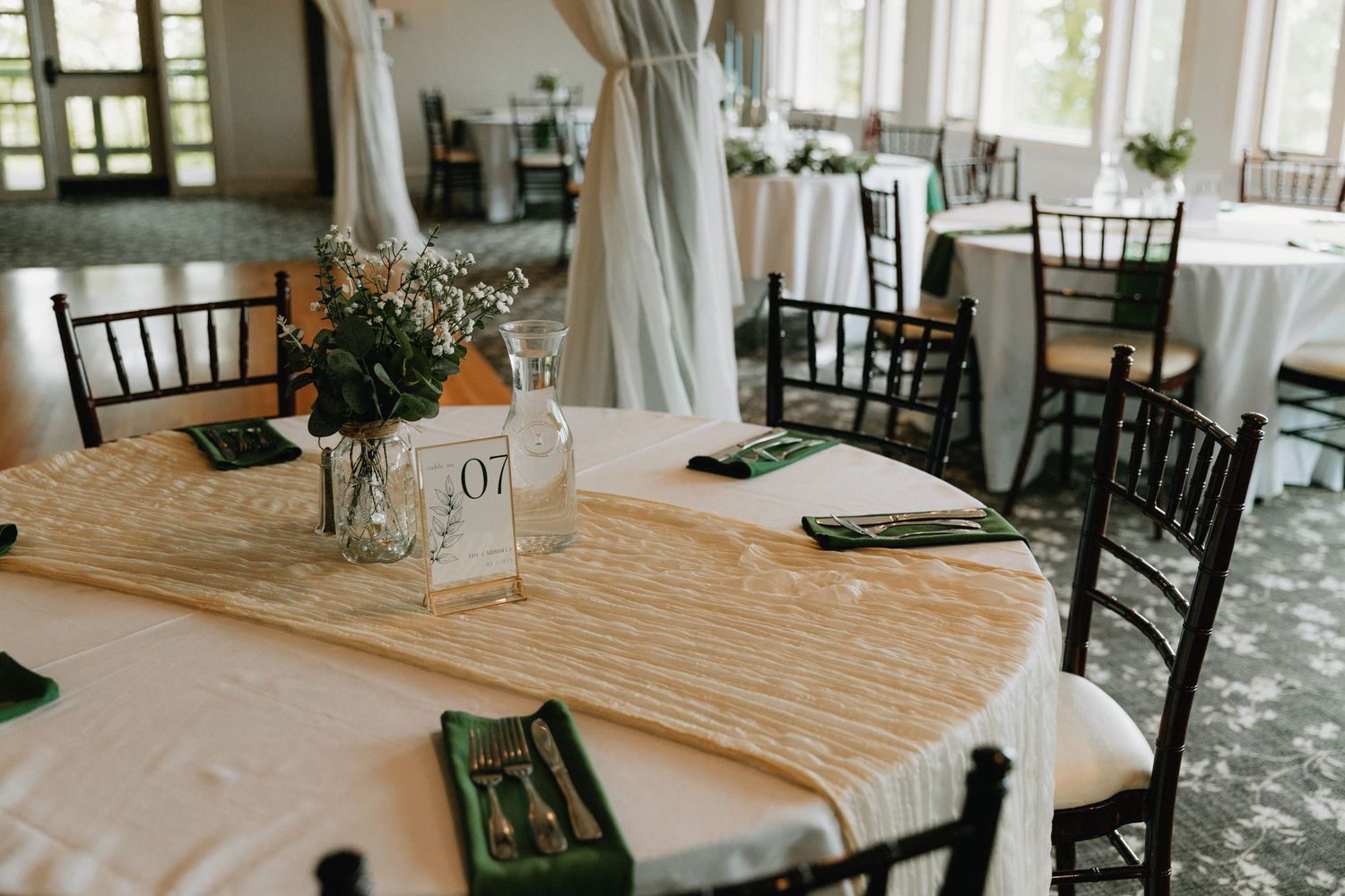 Wedding reception venue with elegant table settings featuring black chairs and white linens.
