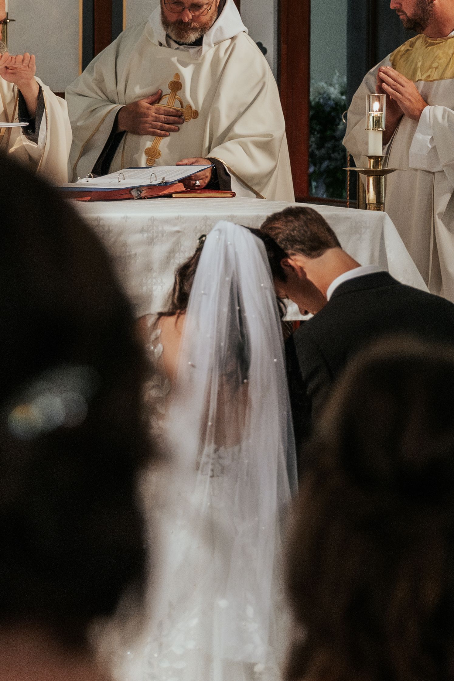 A close-up view of a Catholic wedding ceremony with priests in white robes performing religious rituals at the altar.