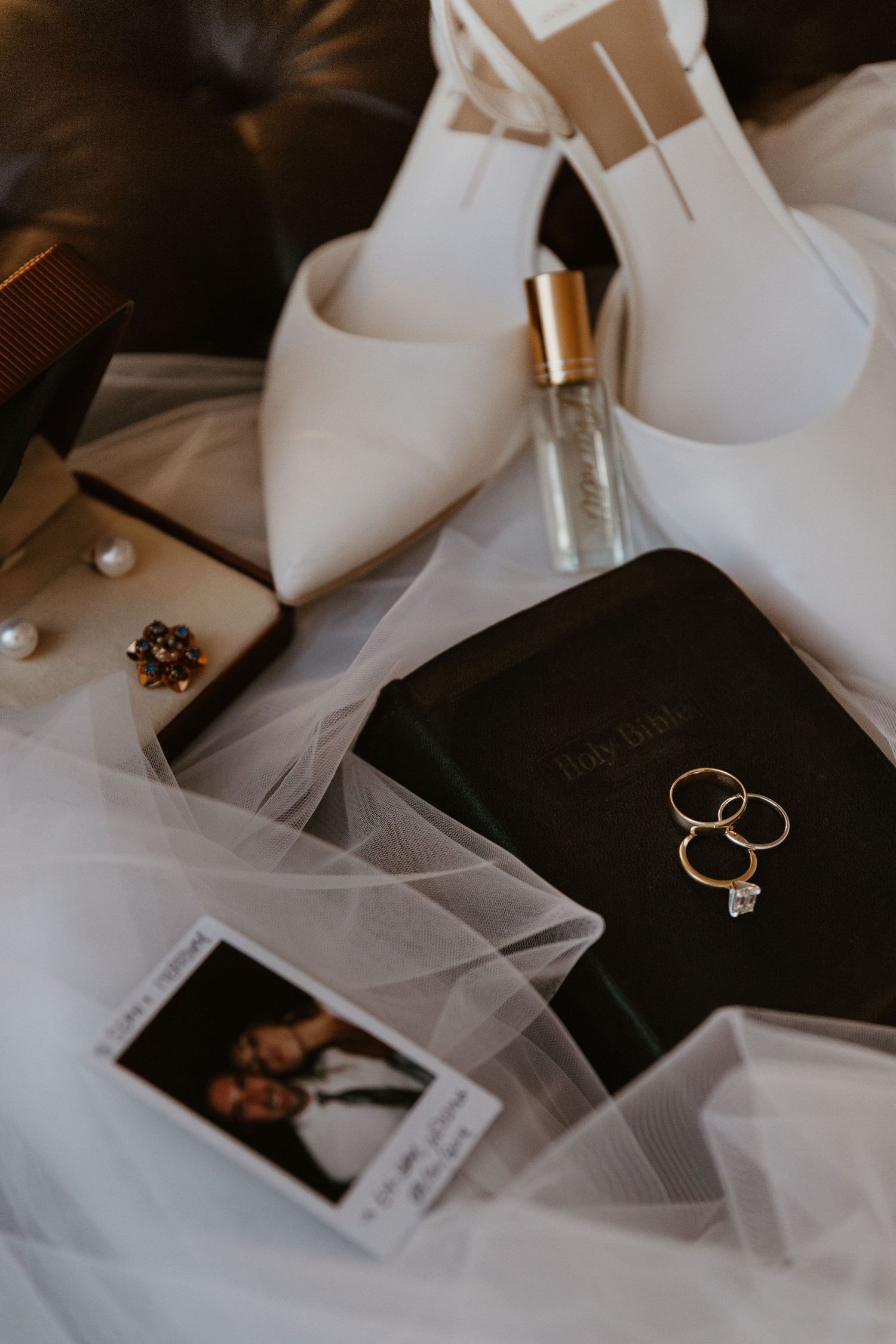 A series of elegant wedding detail shots showing white shoes, veil, perfume bottle, and gold wedding rings on dark surfaces.