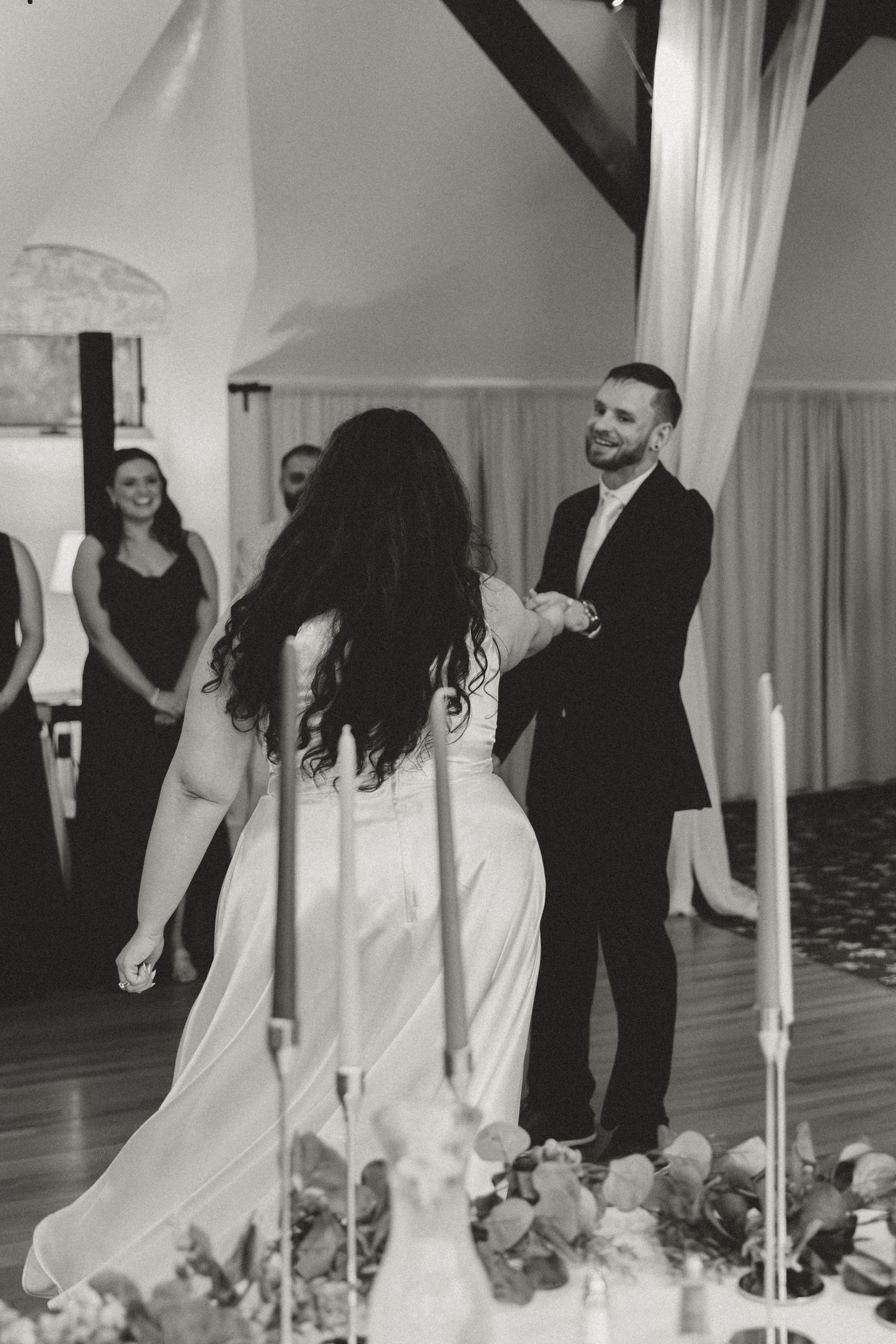 A couple shares their first dance in an elegant reception hall with white drapes and candlelight.