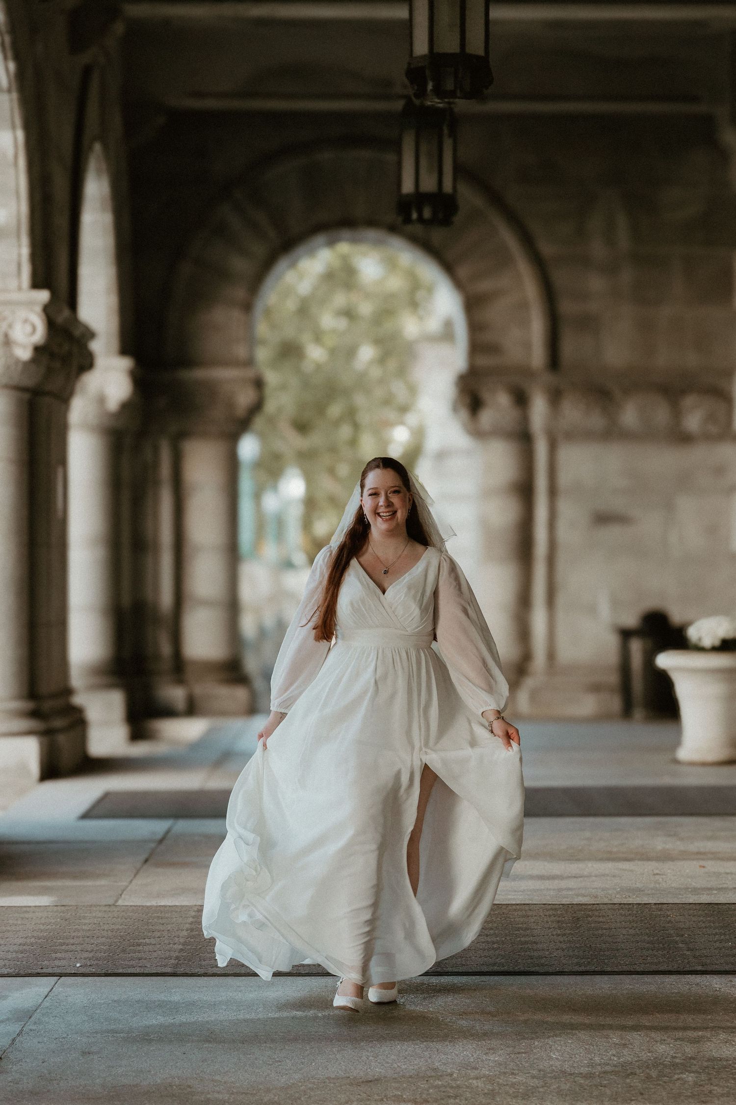 Bride in flowing white dress walks through elegant stone archway.