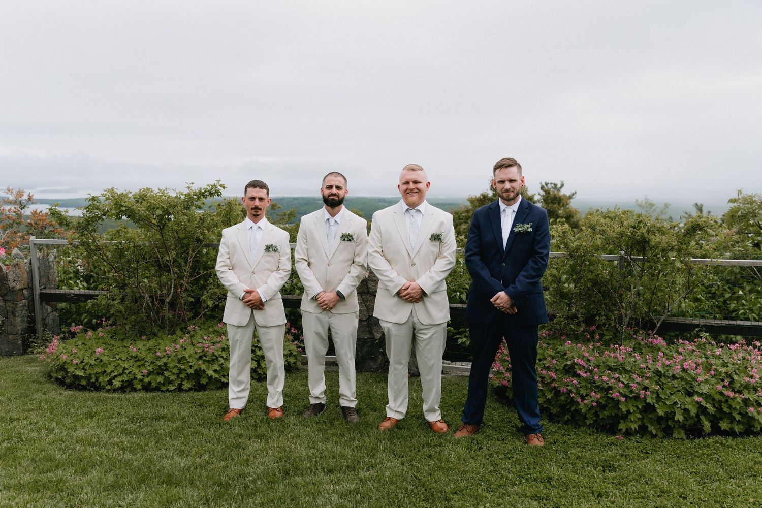 Groomsmen in white and navy suits posing outdoors at wedding venue.