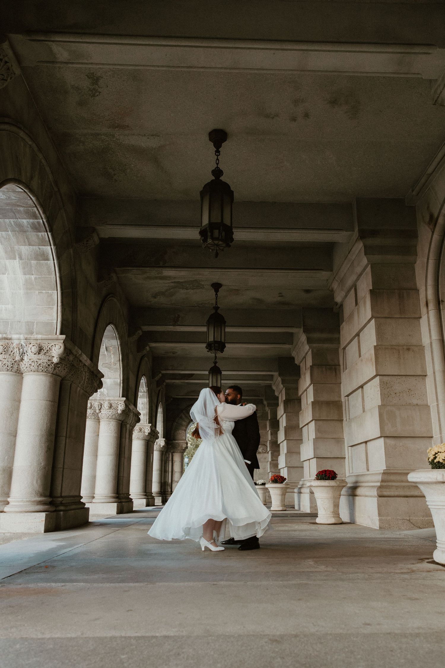 A bride in a flowing white gown walks through an elegant columned passageway.