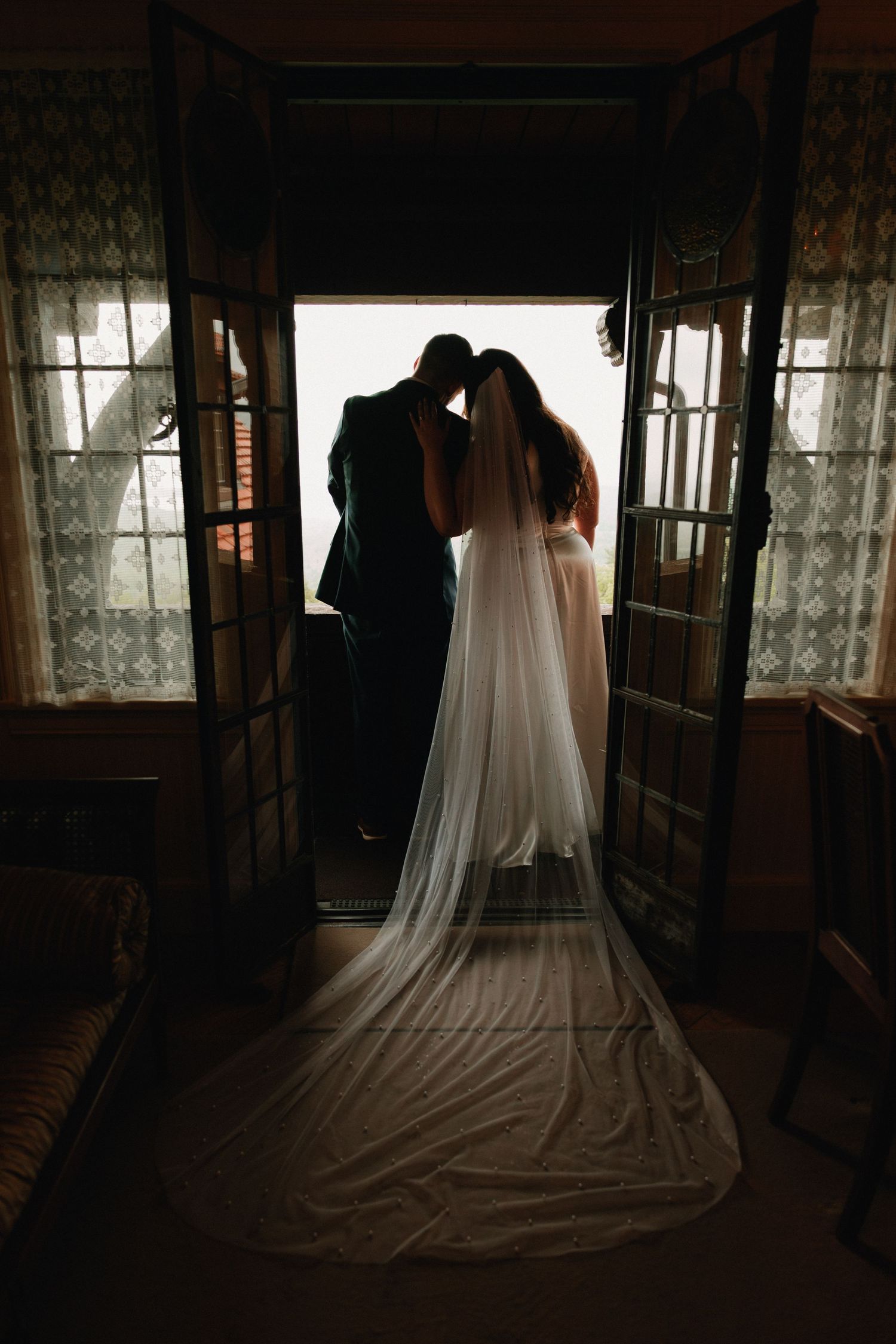 Silhouette of wedding dress and veil against window light in rustic interior.