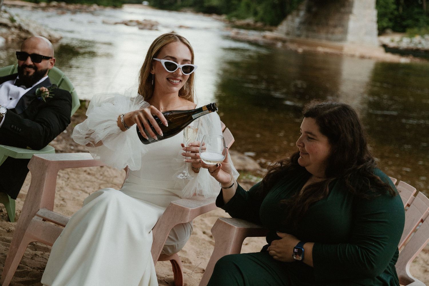 Wedding party enjoying champagne and celebrations by a riverbank.