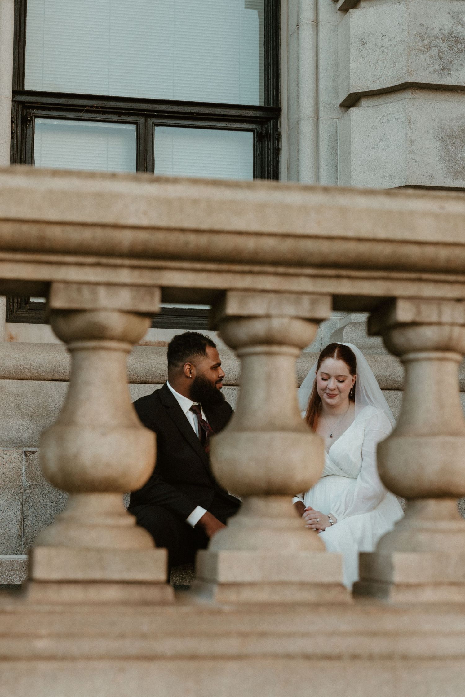 A couple shares an intimate moment between stone balustrades on their wedding day.
