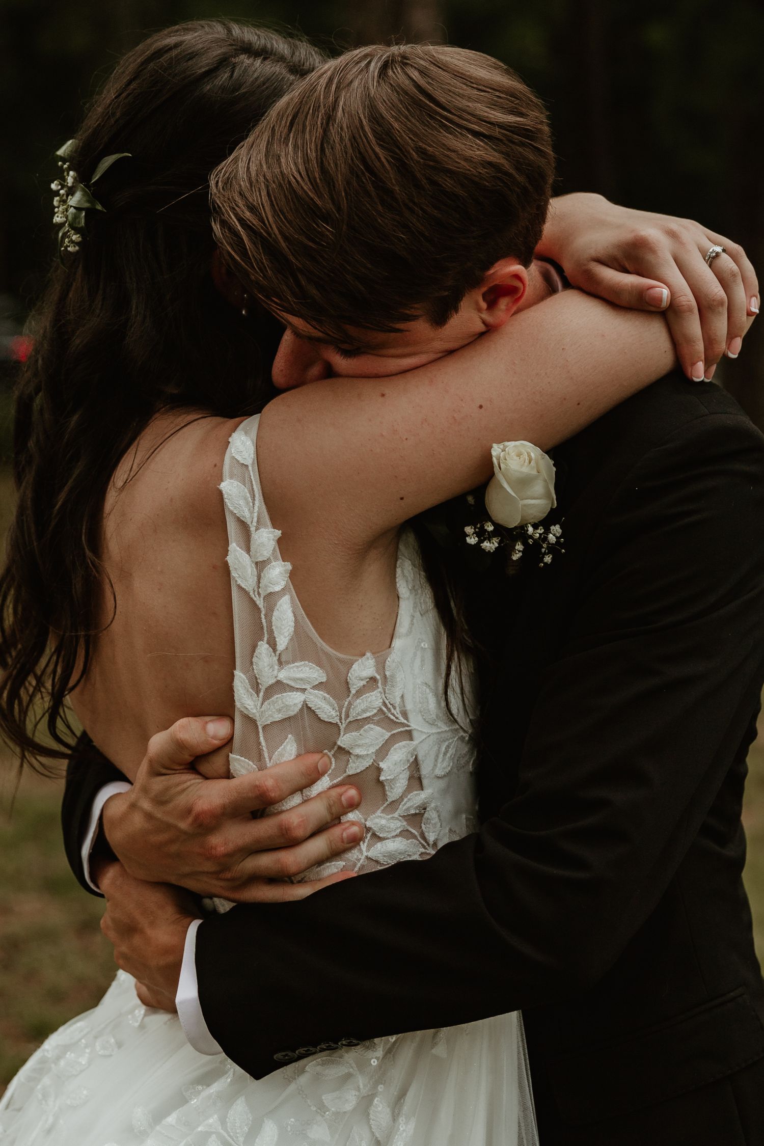 A romantic embrace between newlyweds showing details of a white lace wedding dress against a dark suit in moody lighting.