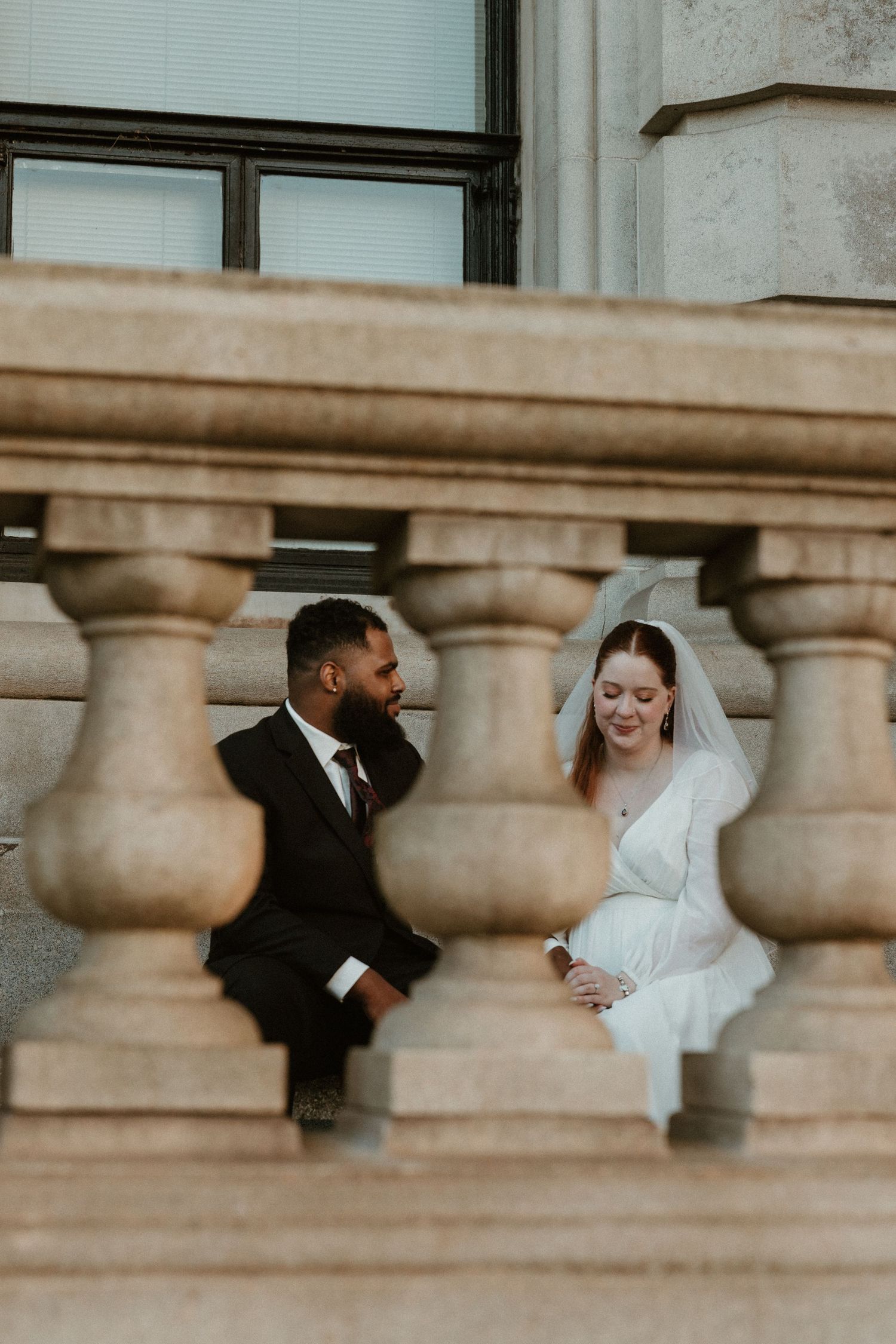Couple shares intimate moment sitting between stone balustrades.