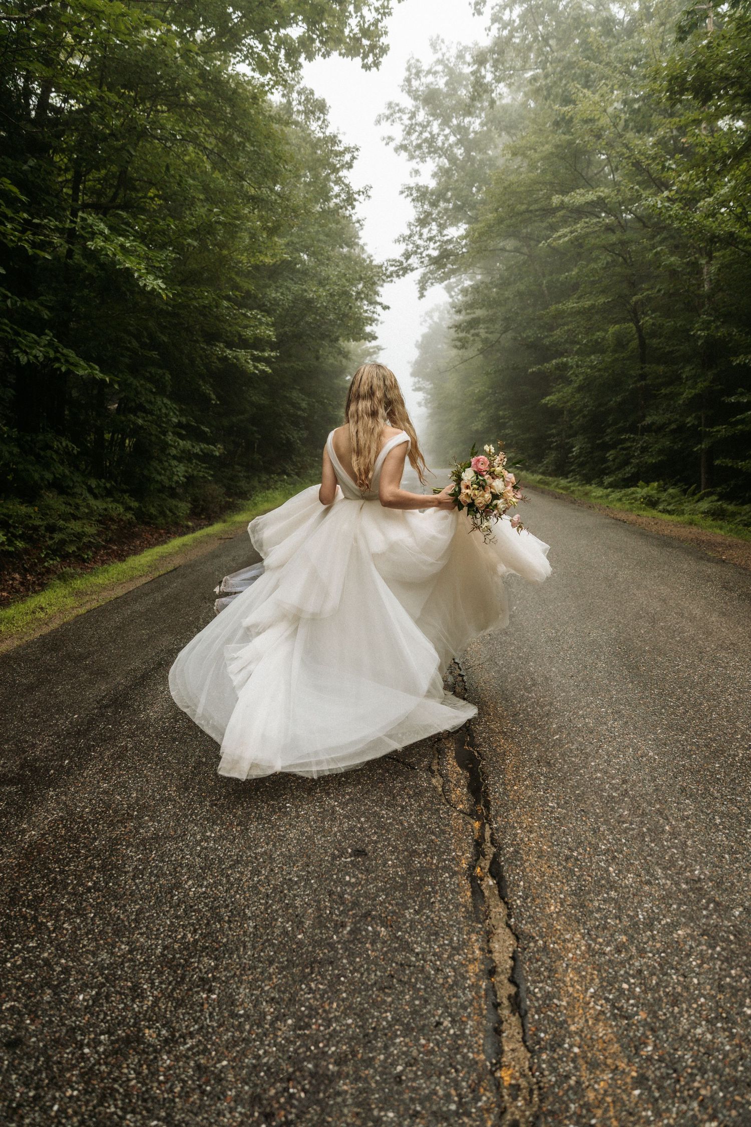 A bride twirls her dress on a misty forest road creating a dreamy effect.