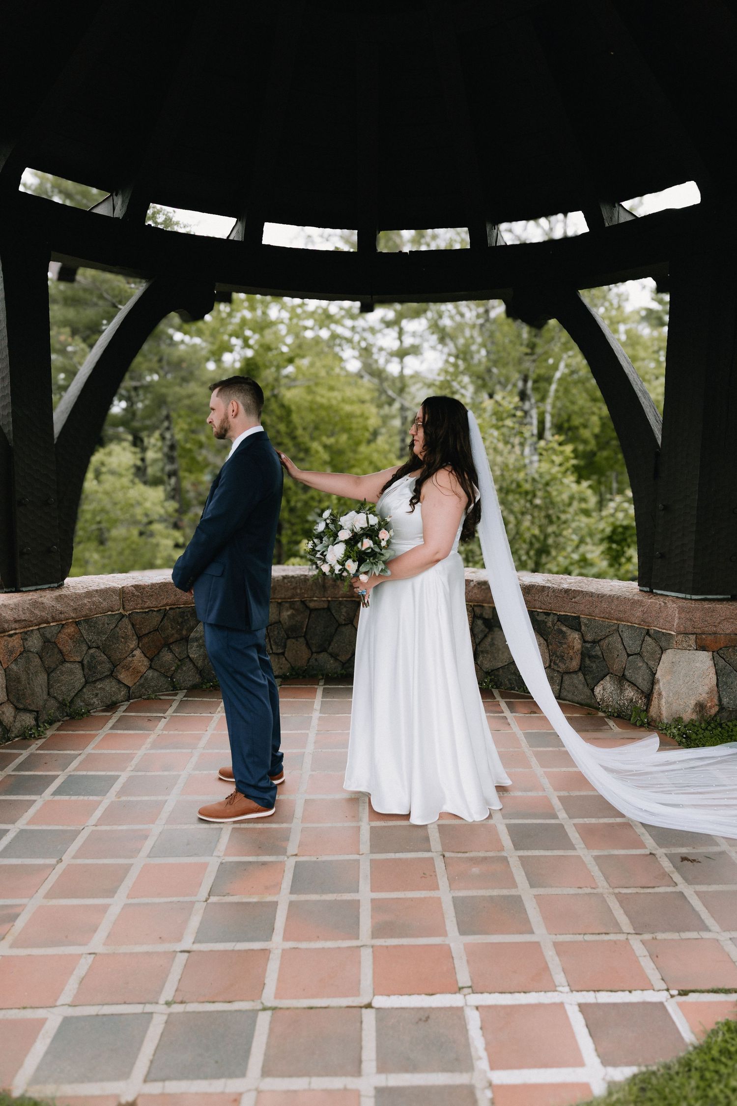 A couple shares their first look moment under a covered pavilion with terracotta tile flooring.