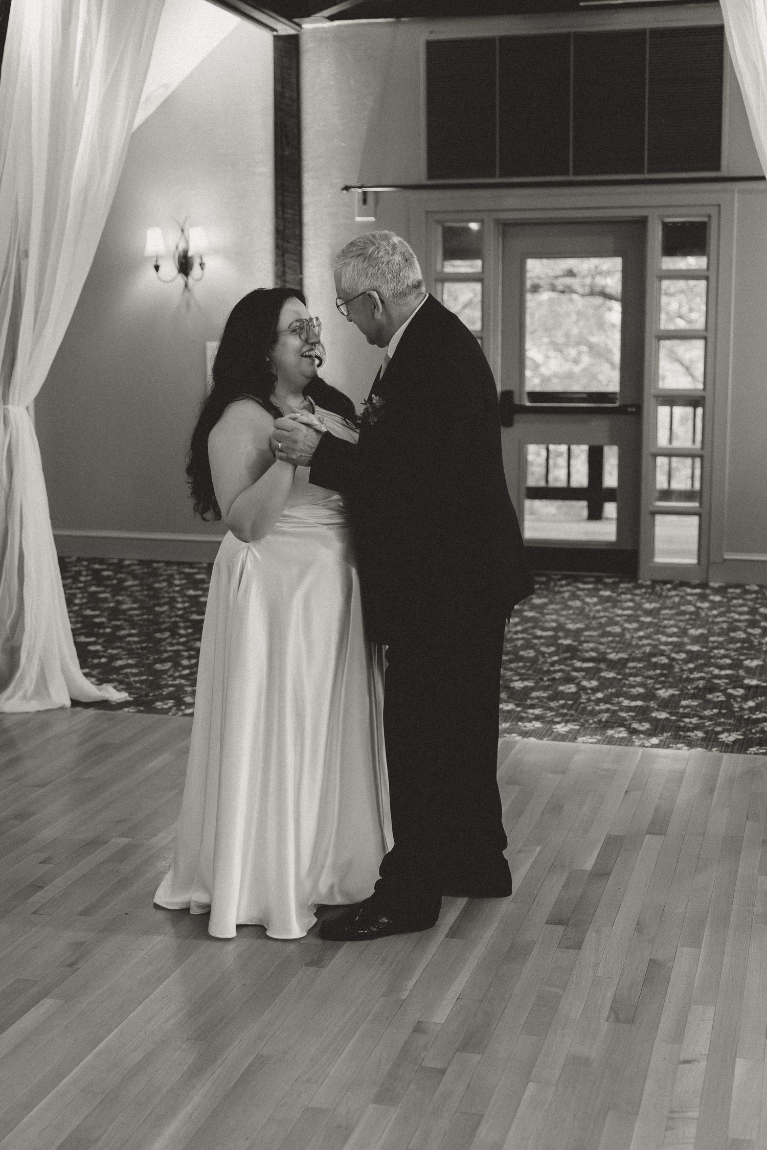 A black and white photo captures an intimate dance moment in an elegant reception venue.