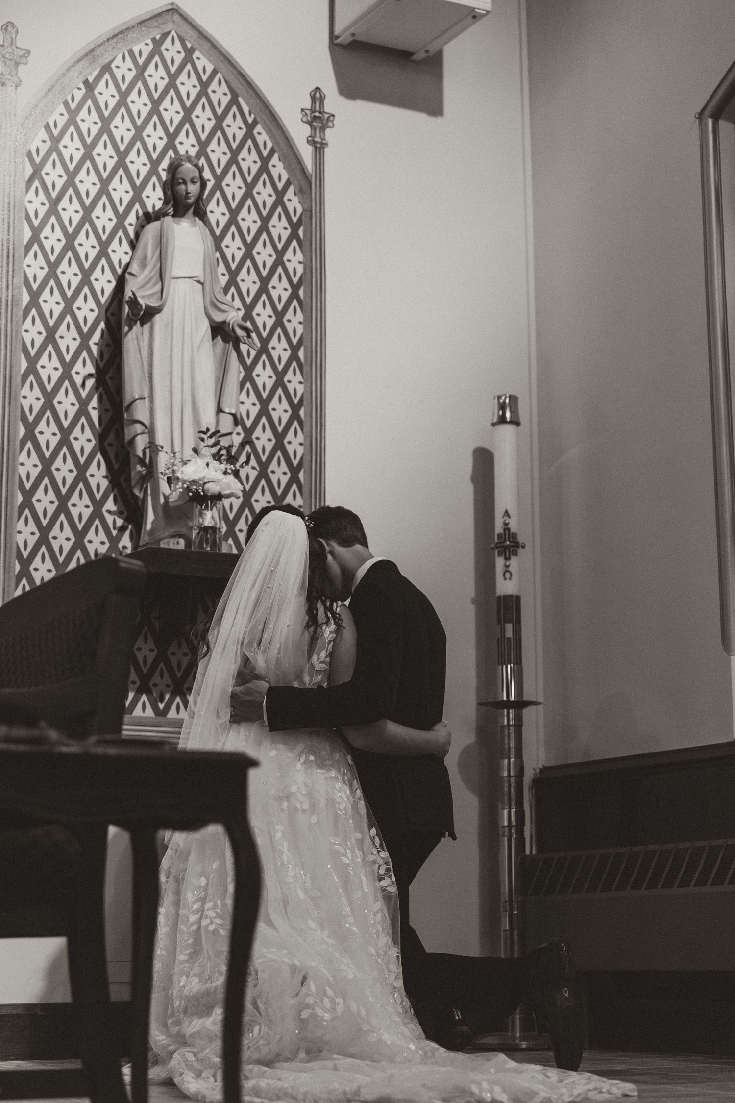 A dramatic black and white wedding photo taken inside a church with ornate diamond-patterned windows.