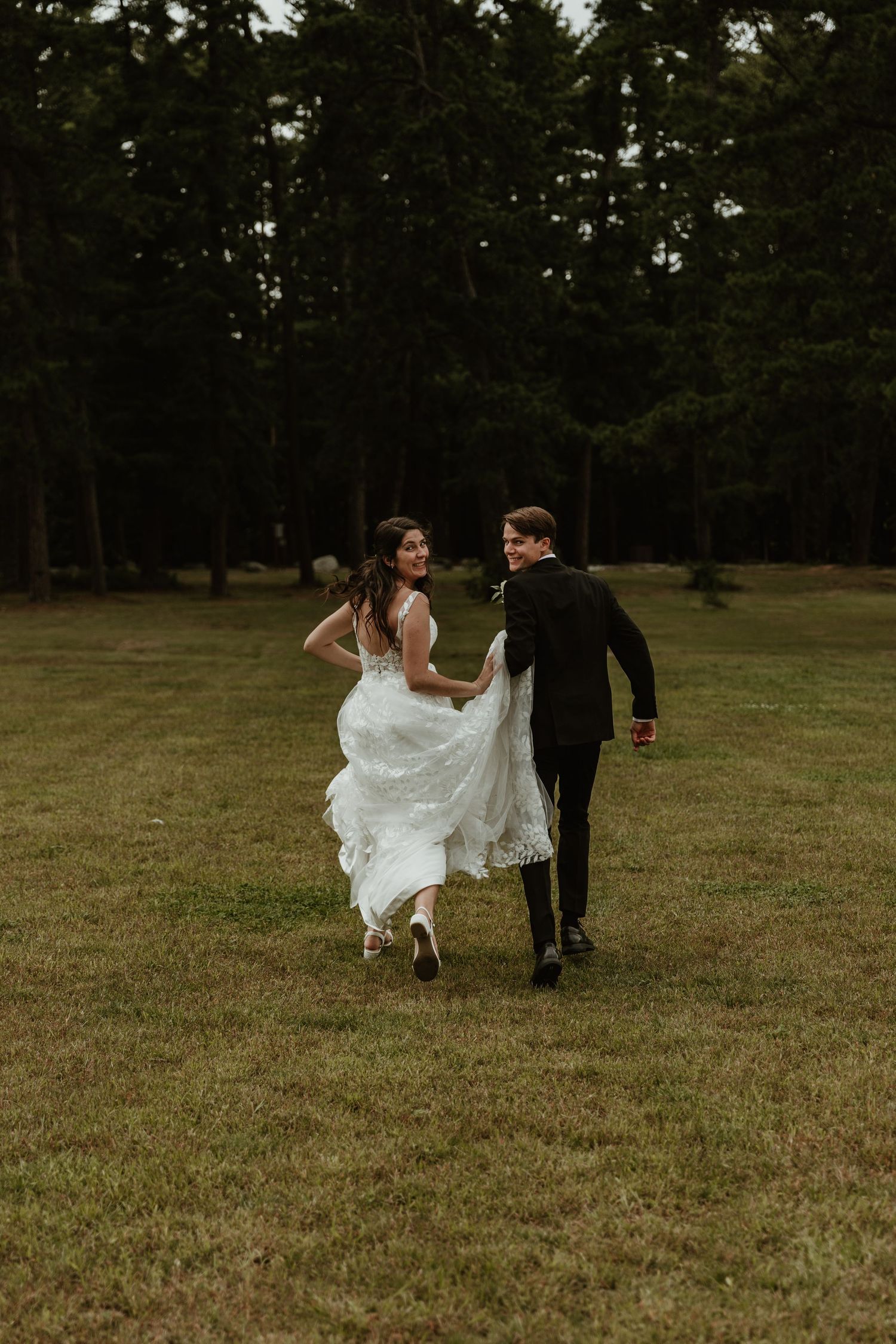 Newlyweds run playfully across a grassy field at their outdoor wedding.