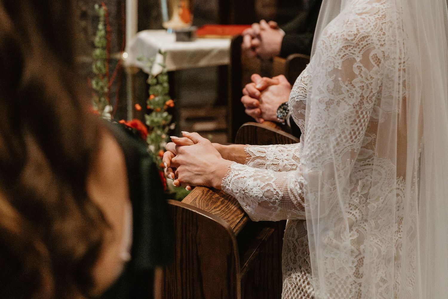 Detail shot of lace wedding dress and veil during church ceremony.