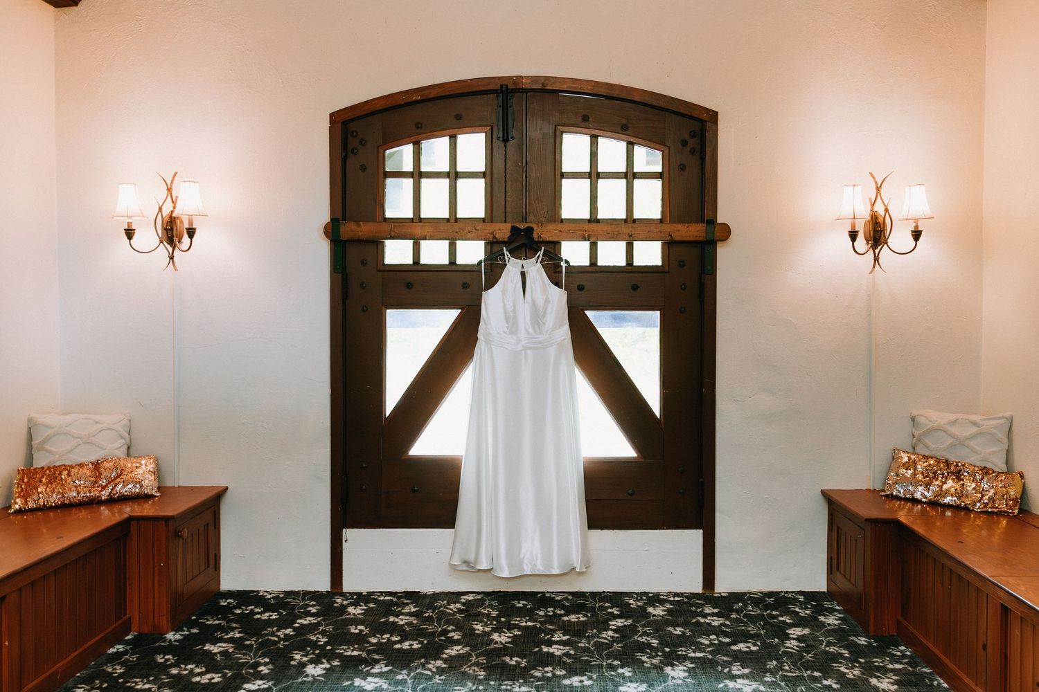 A wedding dress hangs elegantly in a room with arched windows and warm lighting.