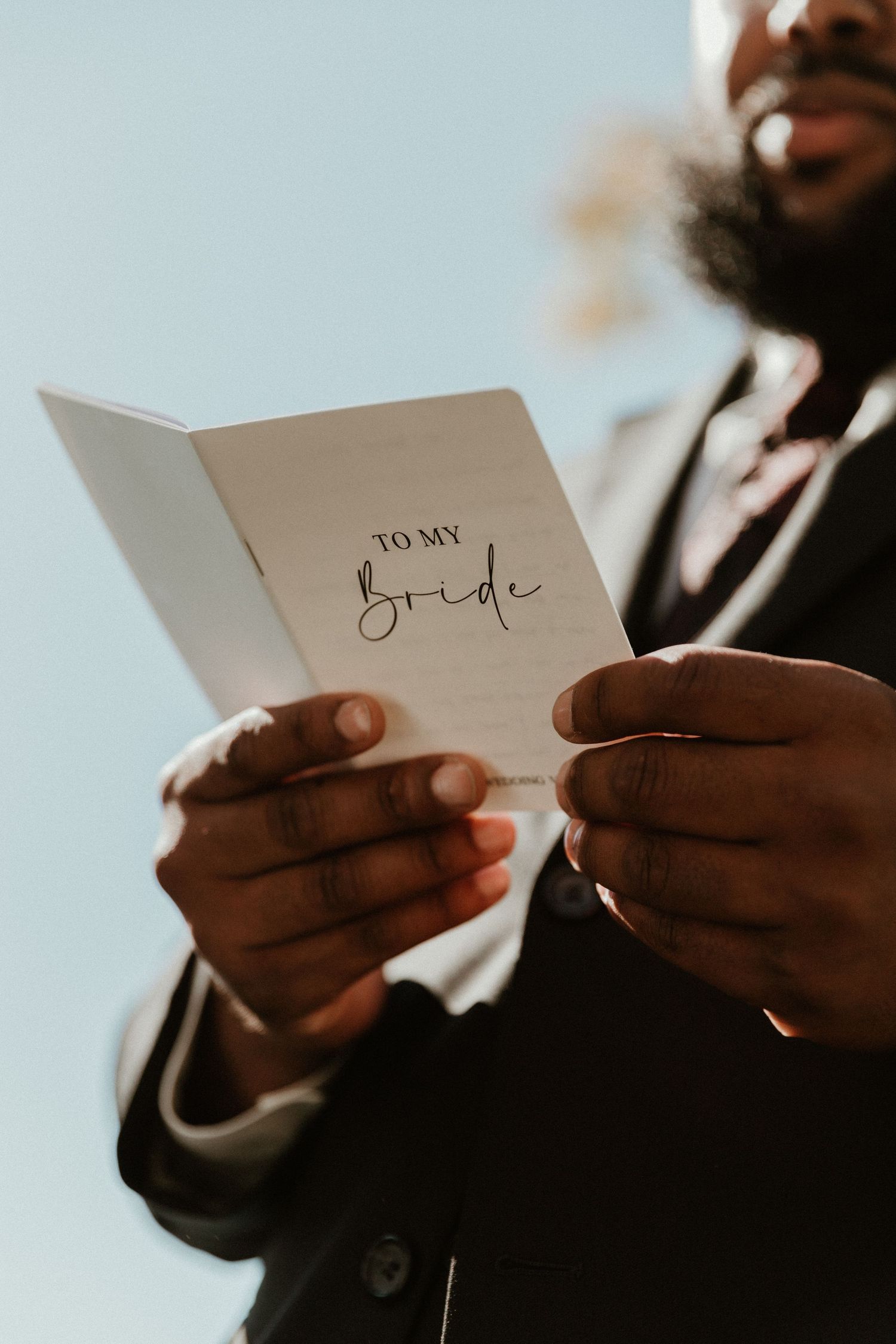 Hands hold a white book titled 'To My Bride' against a bright blue sky.