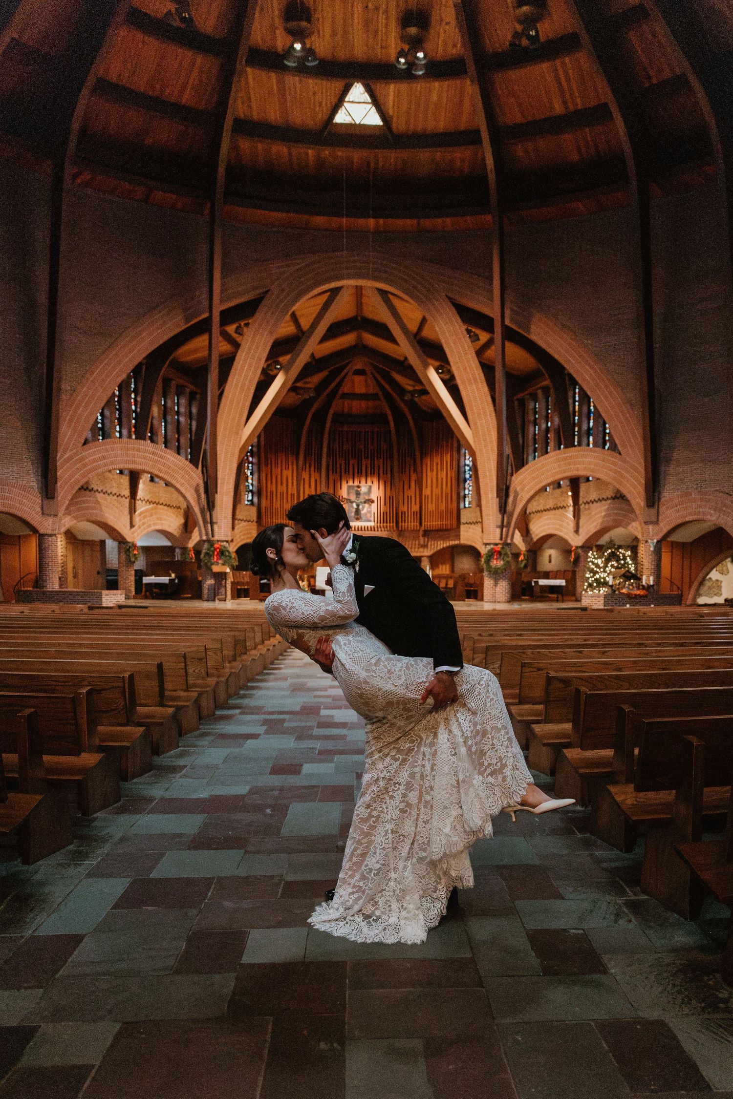 A romantic wedding moment in a stunning cathedral with dramatic wooden arches and vaulted ceilings.