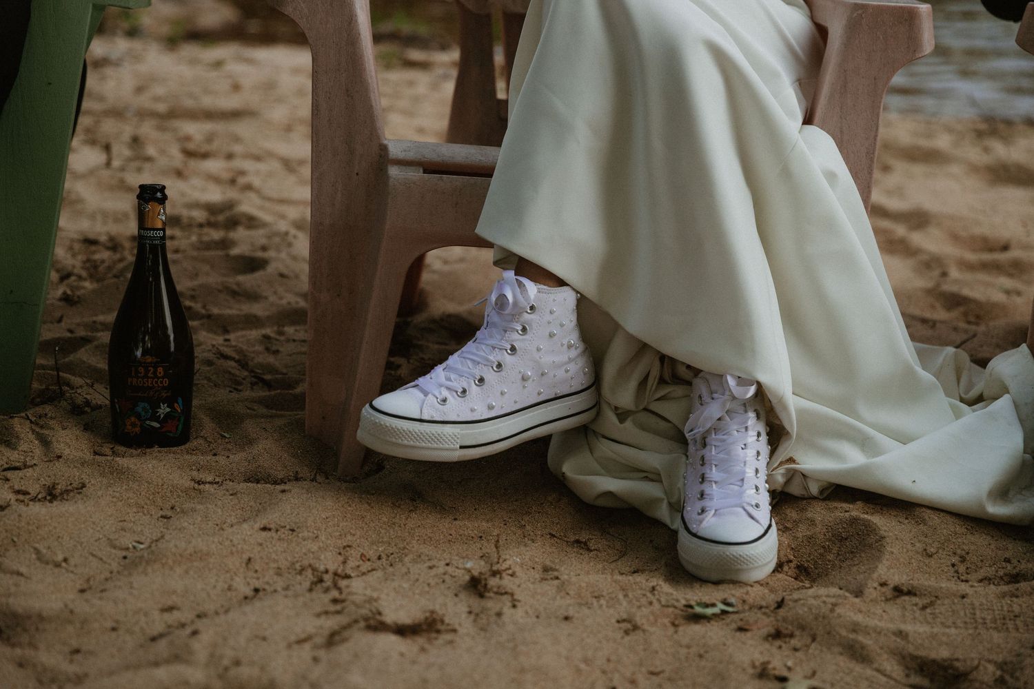 White sneakers and dress shoes lined up on a sandy beach for a wedding photo.