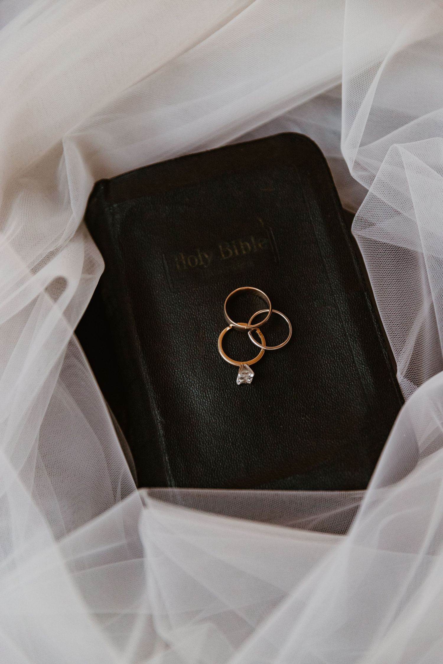 Wedding rings and engagement ring displayed on black velvet against soft white tulle fabric background.