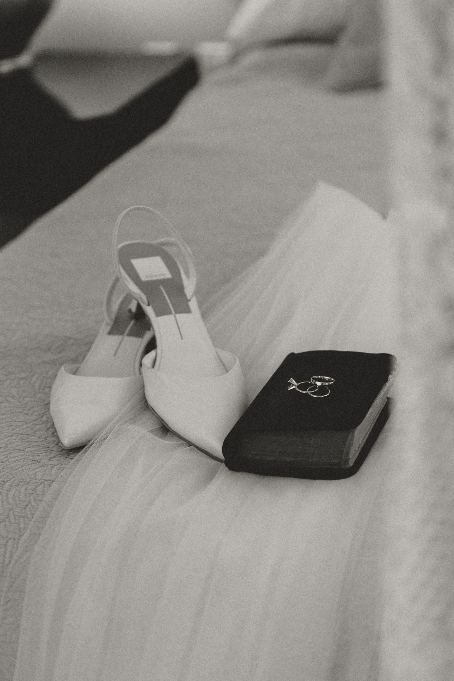 Black and white detail shot of wedding rings and accessories on a textured surface.