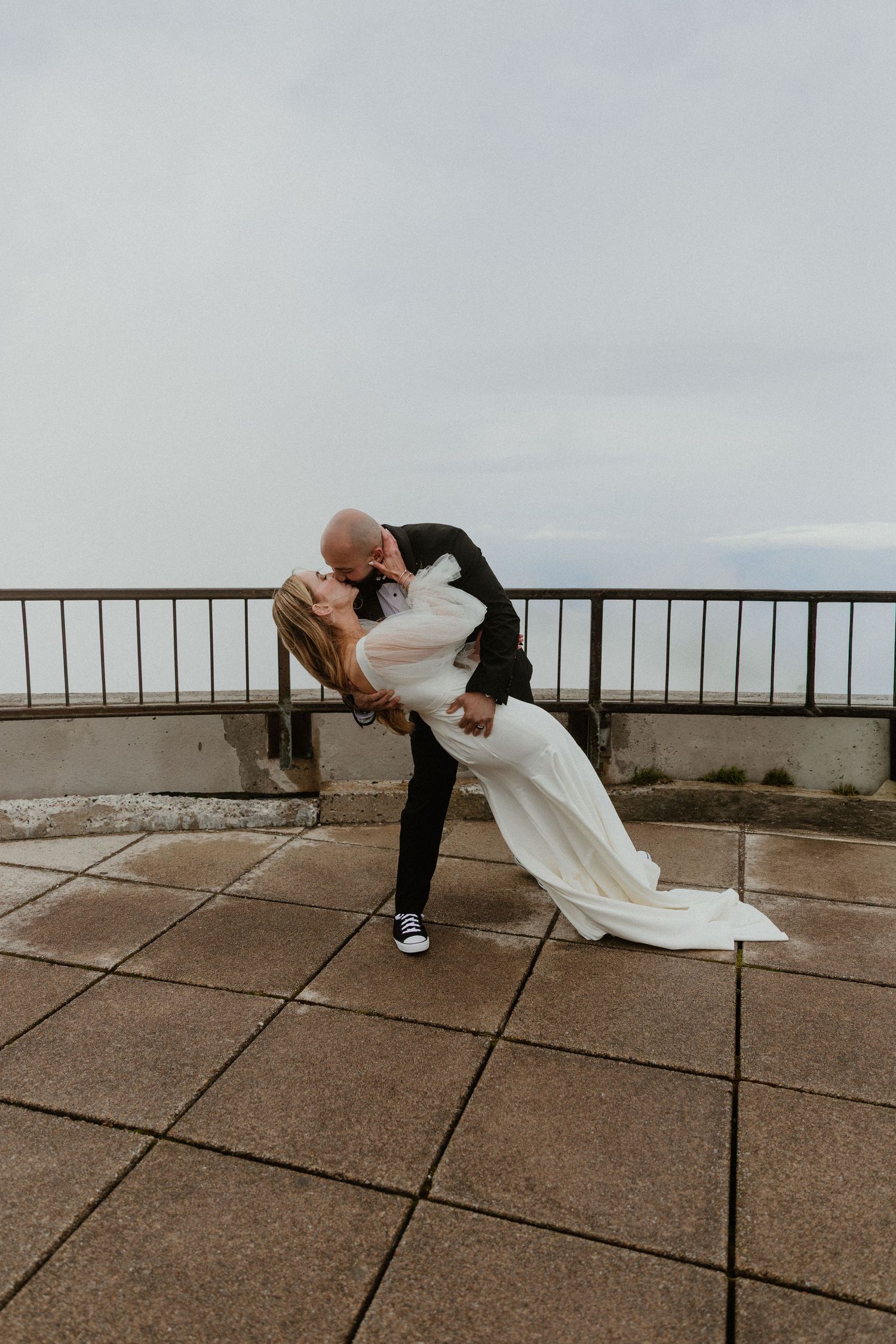 Dramatic wedding pose on concrete terrace with scenic mountain backdrop.