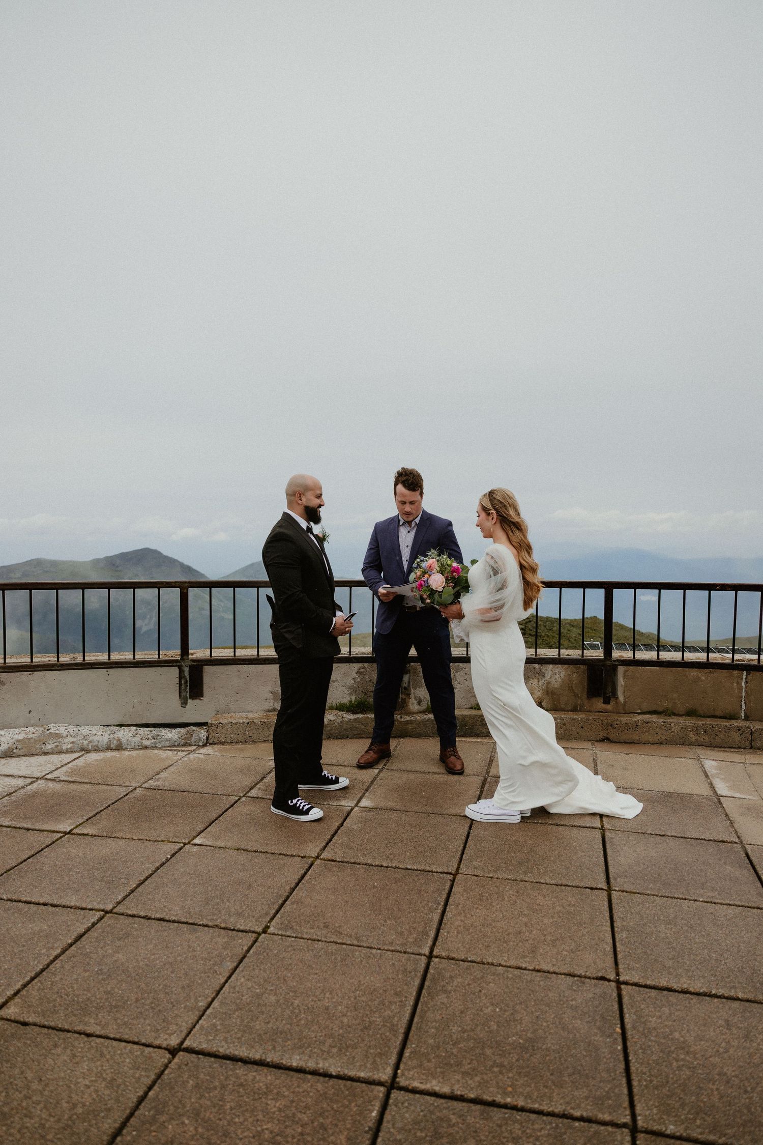 A wedding ceremony takes place on a scenic mountain overlook with stone pavers and distant mountain views in the background.