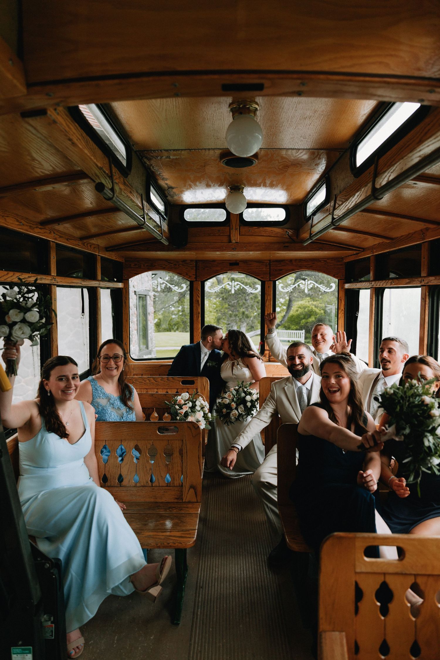 Wedding celebration inside a vintage wooden trolley car with decorative floral arrangements.