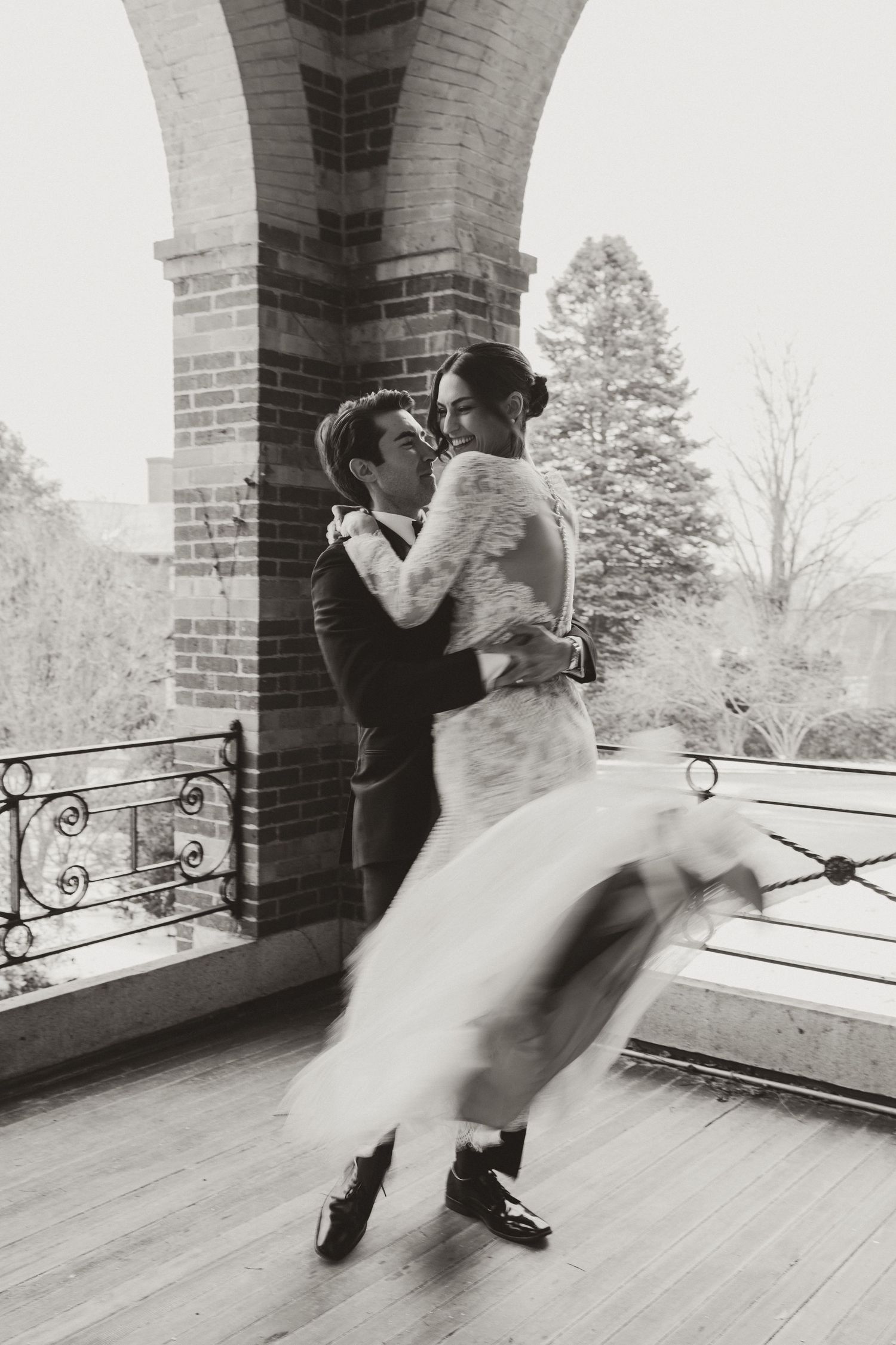 Black and white photo of a couple dancing on a balcony during their wedding.