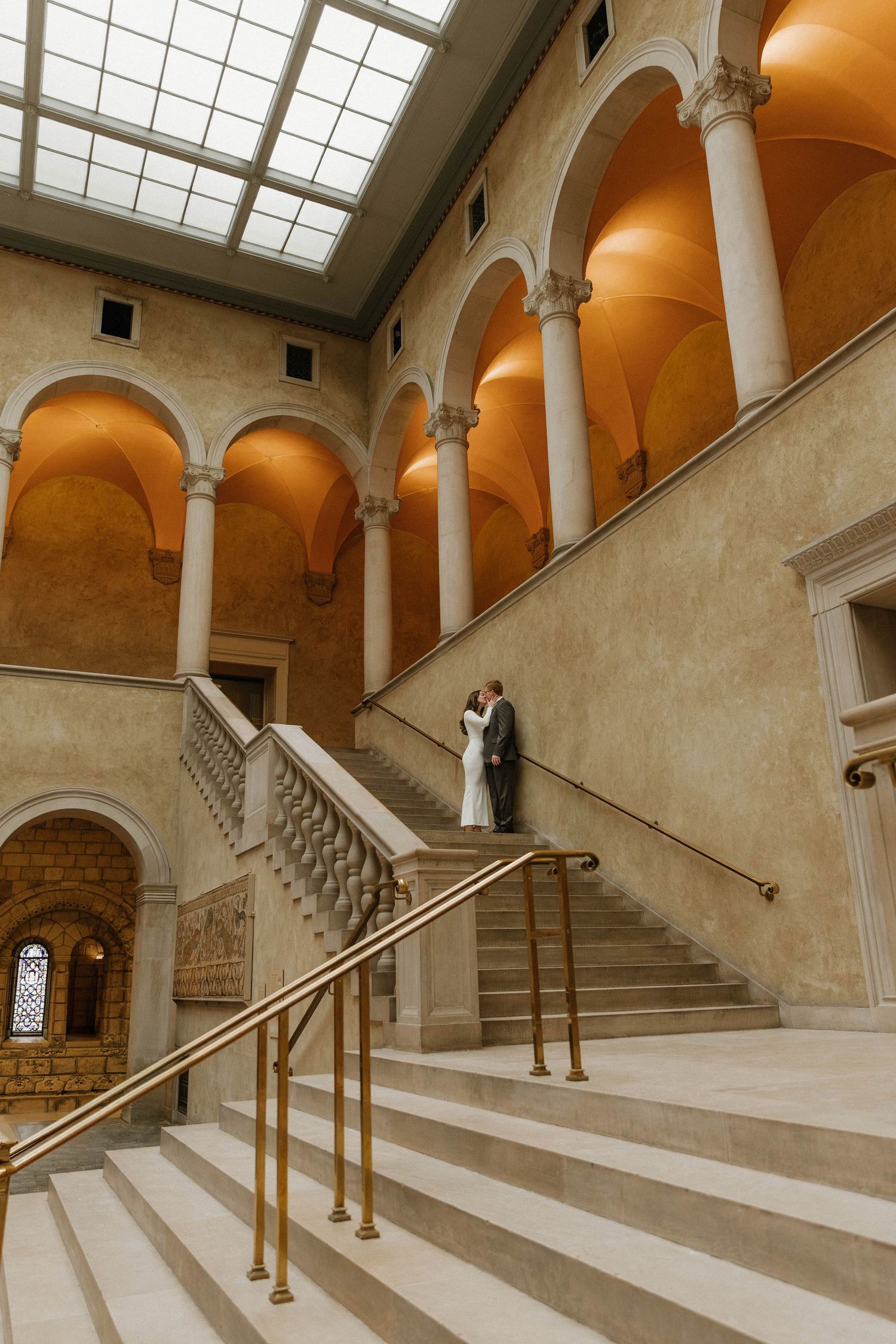 Elegant marble staircase with arched columns and skylights in a grand historic building interior.