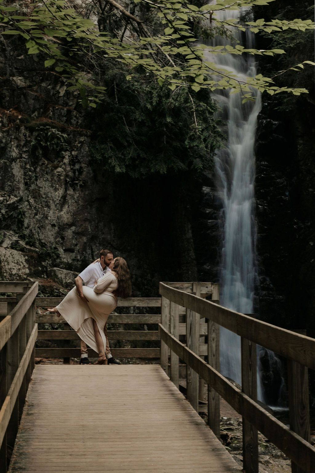 A romantic scene unfolds on a wooden boardwalk with a cascading waterfall in the background.