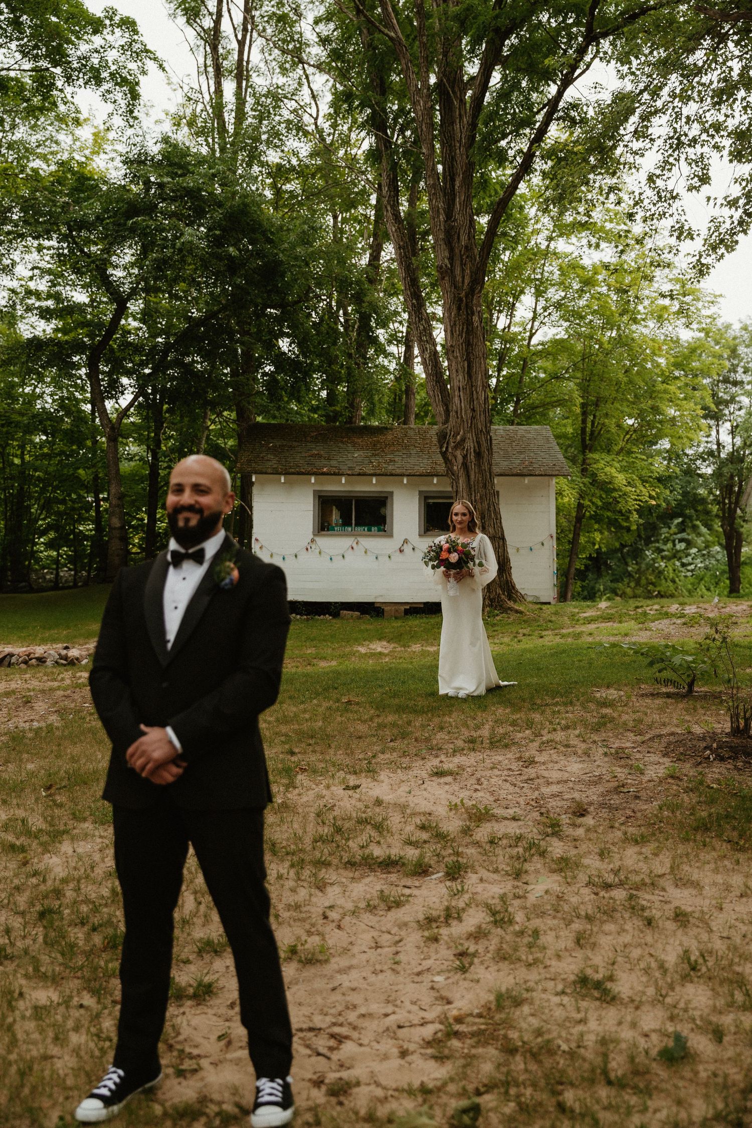Wedding party in formal attire posing in front of a rustic white building.