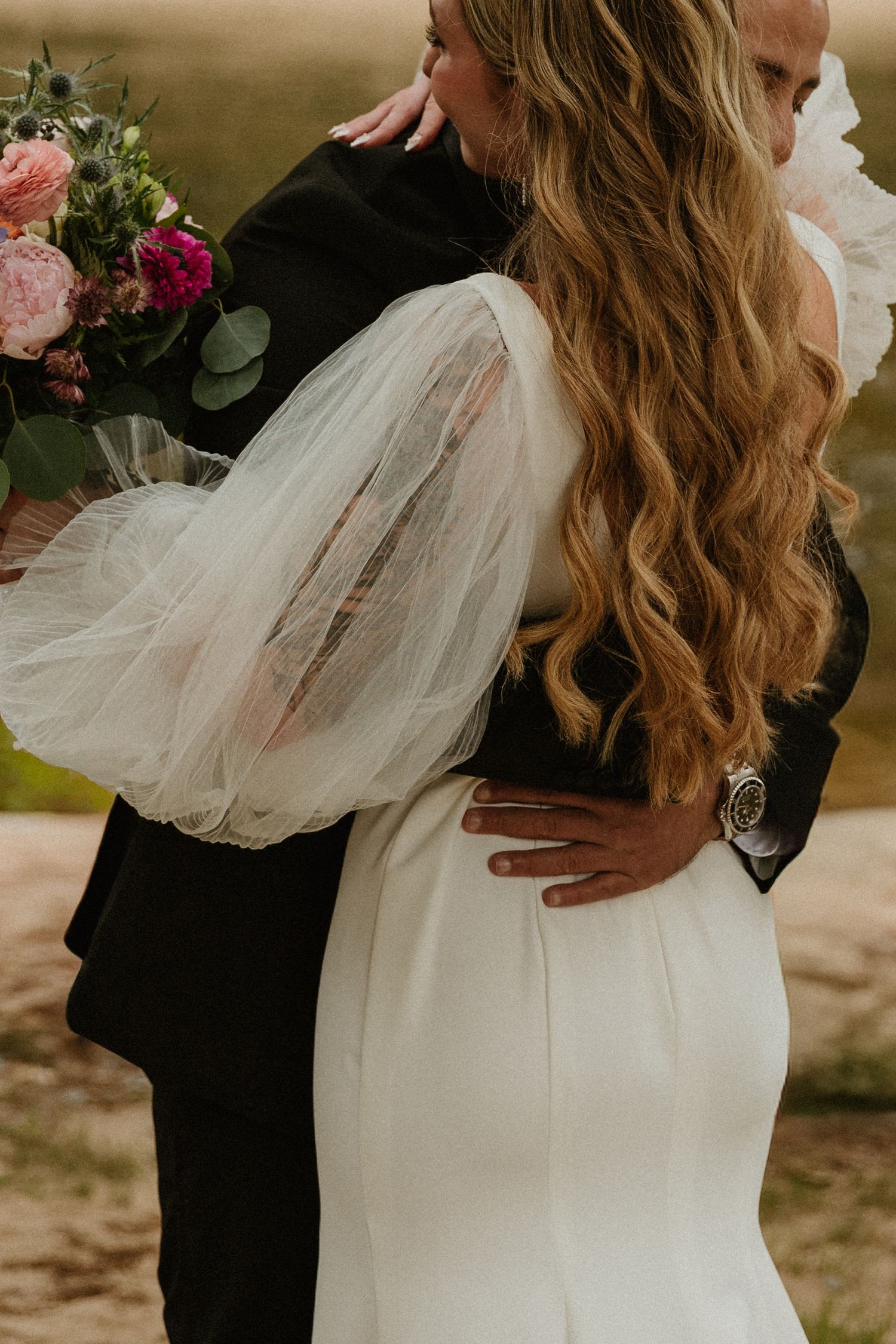 A couple embraces outdoors with the bride wearing a flowing white dress with romantic ruffled details.