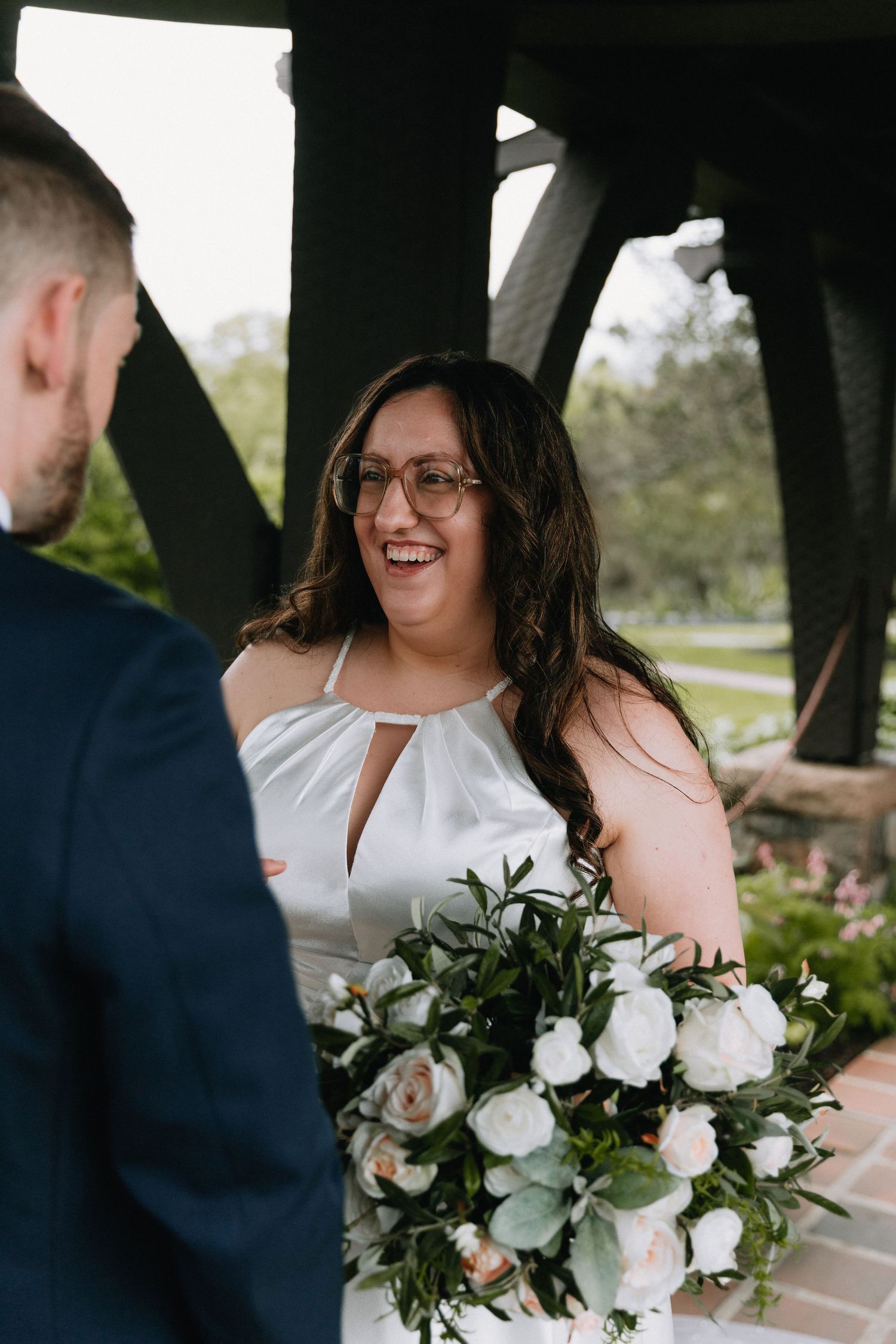 Joyful wedding moment shared under a rustic pavilion with white and pink floral bouquet.