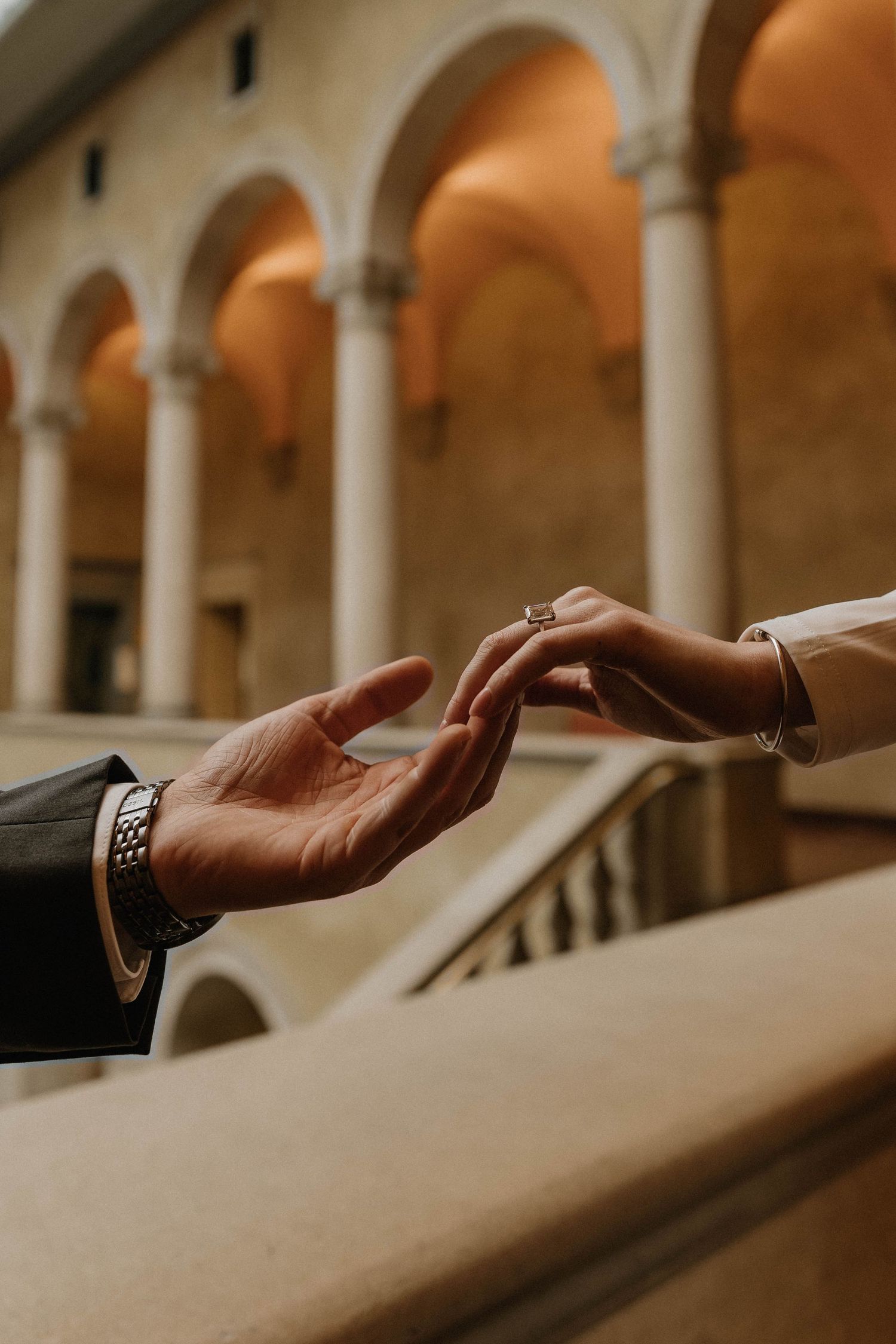 Hands reaching out in sequence across a blurred architectural background with arched columns and warm lighting.